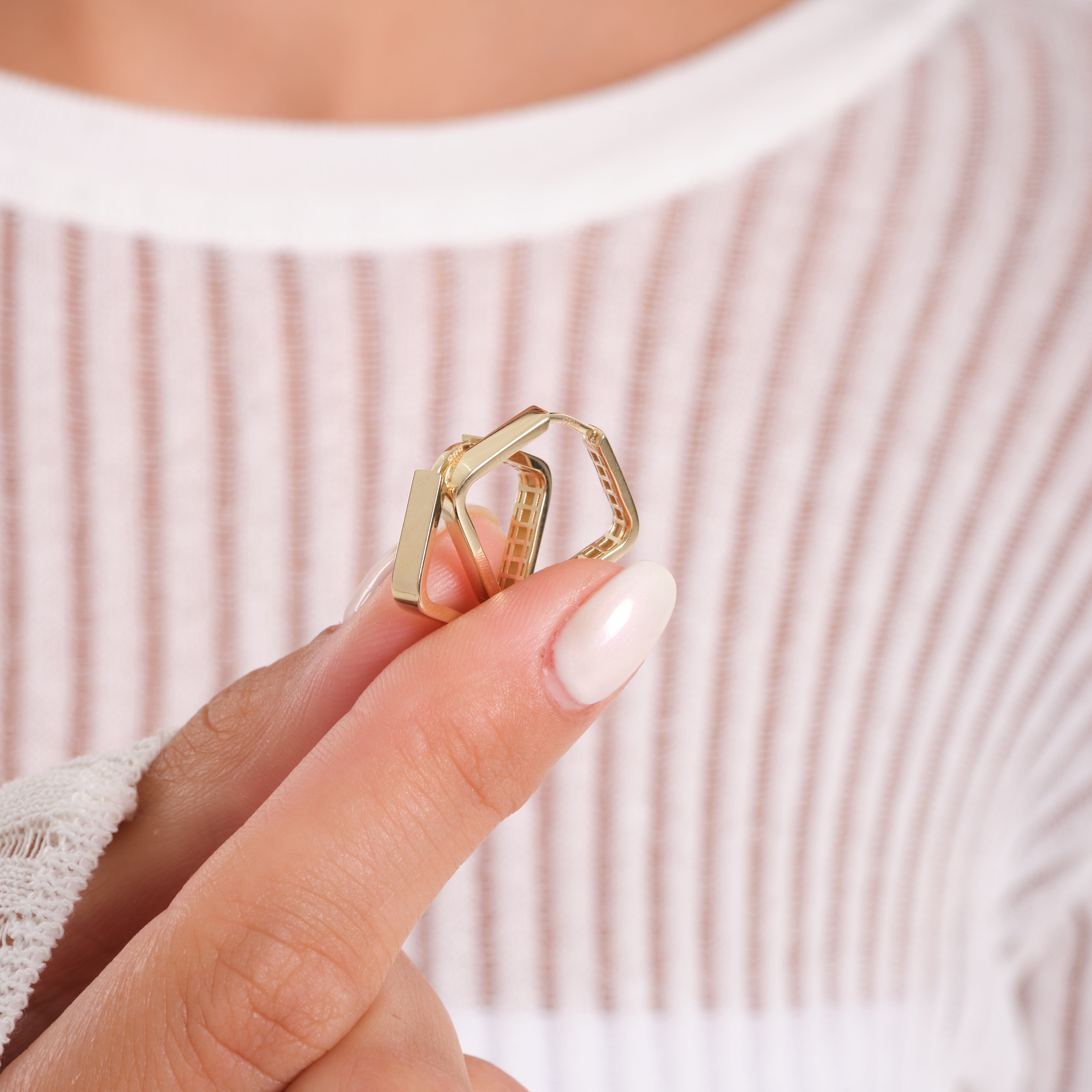 Gold ring with geometric design held by a hand against a blurred background
