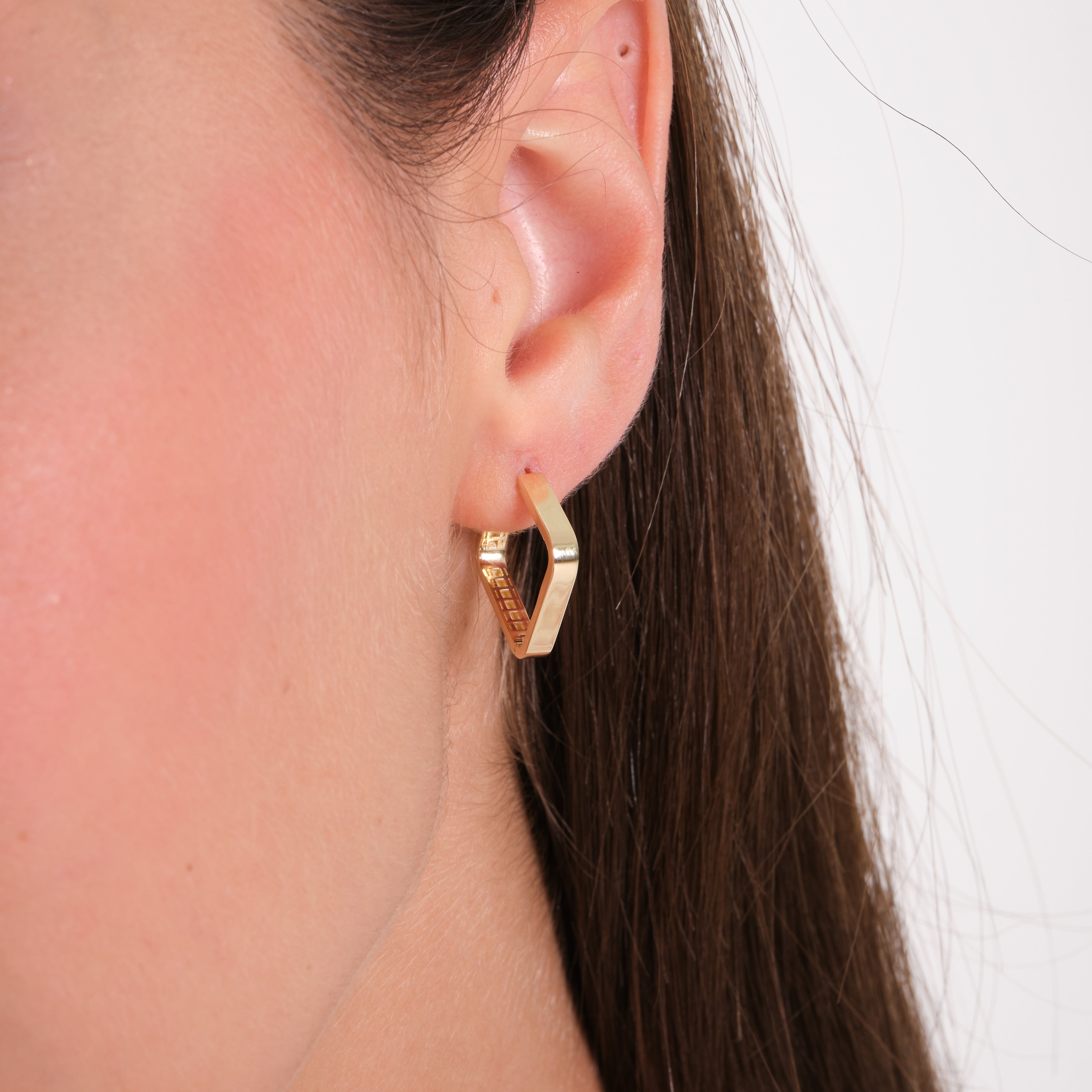 Gold hoop earring worn by a person with a neutral background