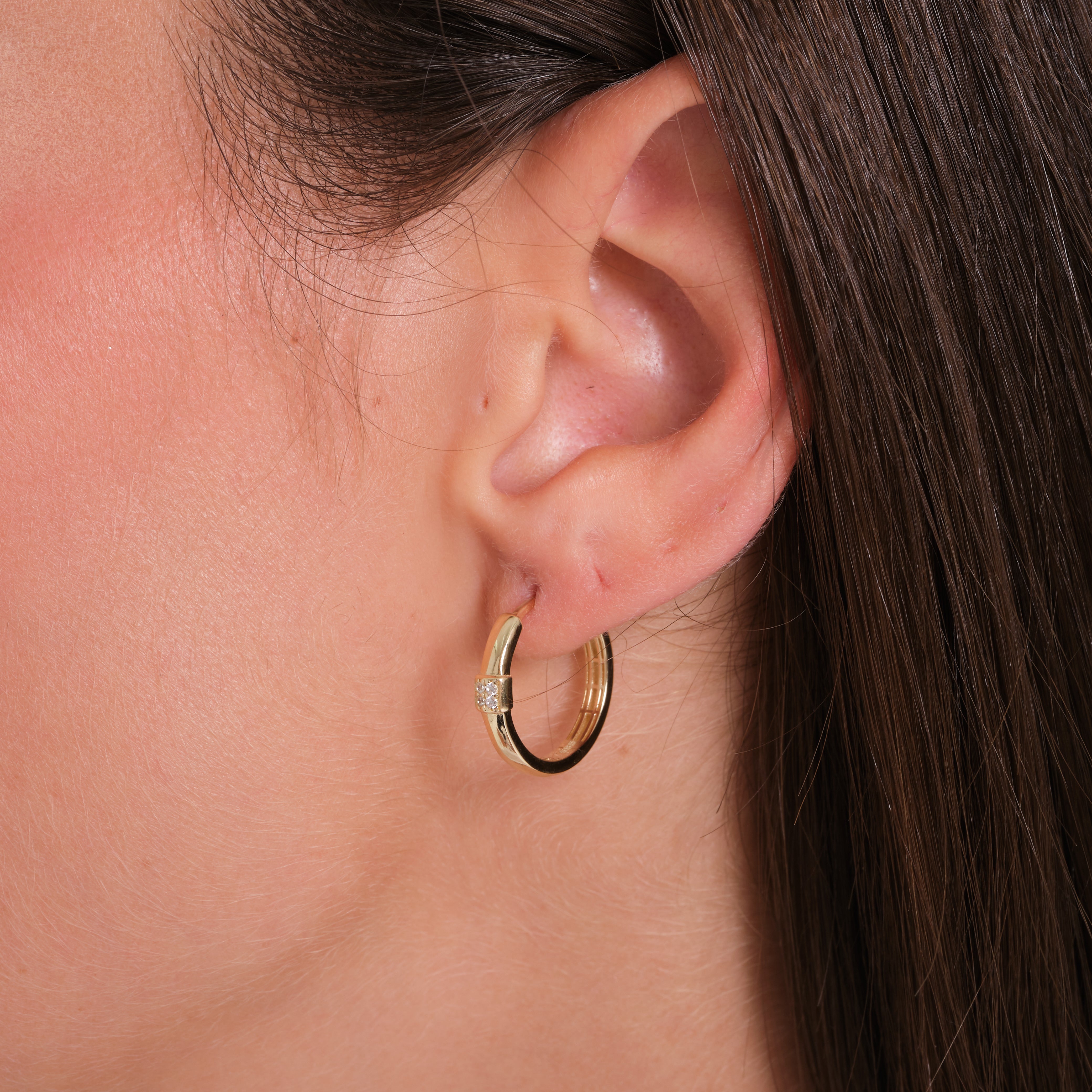 Close-up of an ear wearing a gold hoop earring with clear stones.