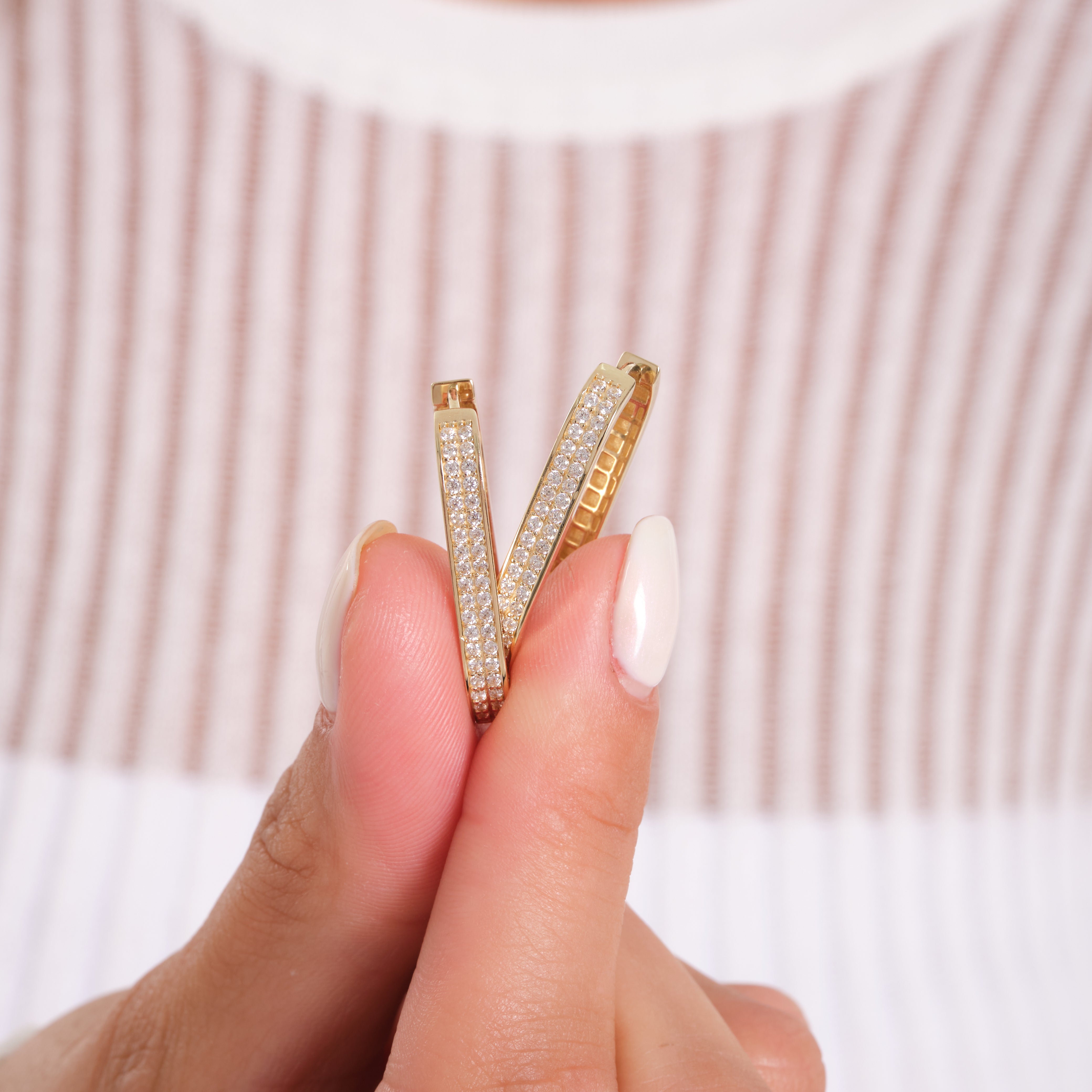 Gold hoop earrings held between fingers against a striped background