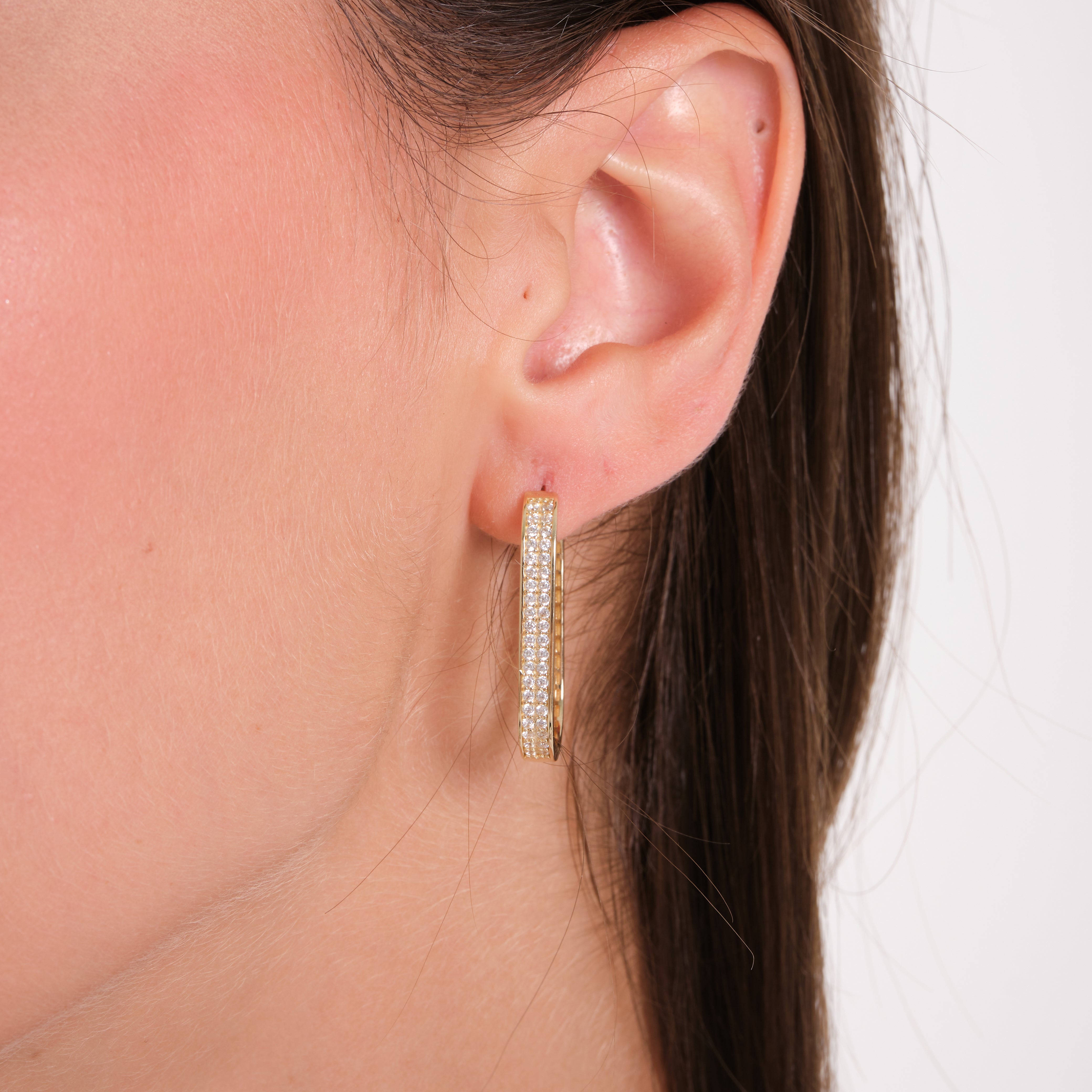 Close-up of an ear wearing a gold hoop earring with a plain background