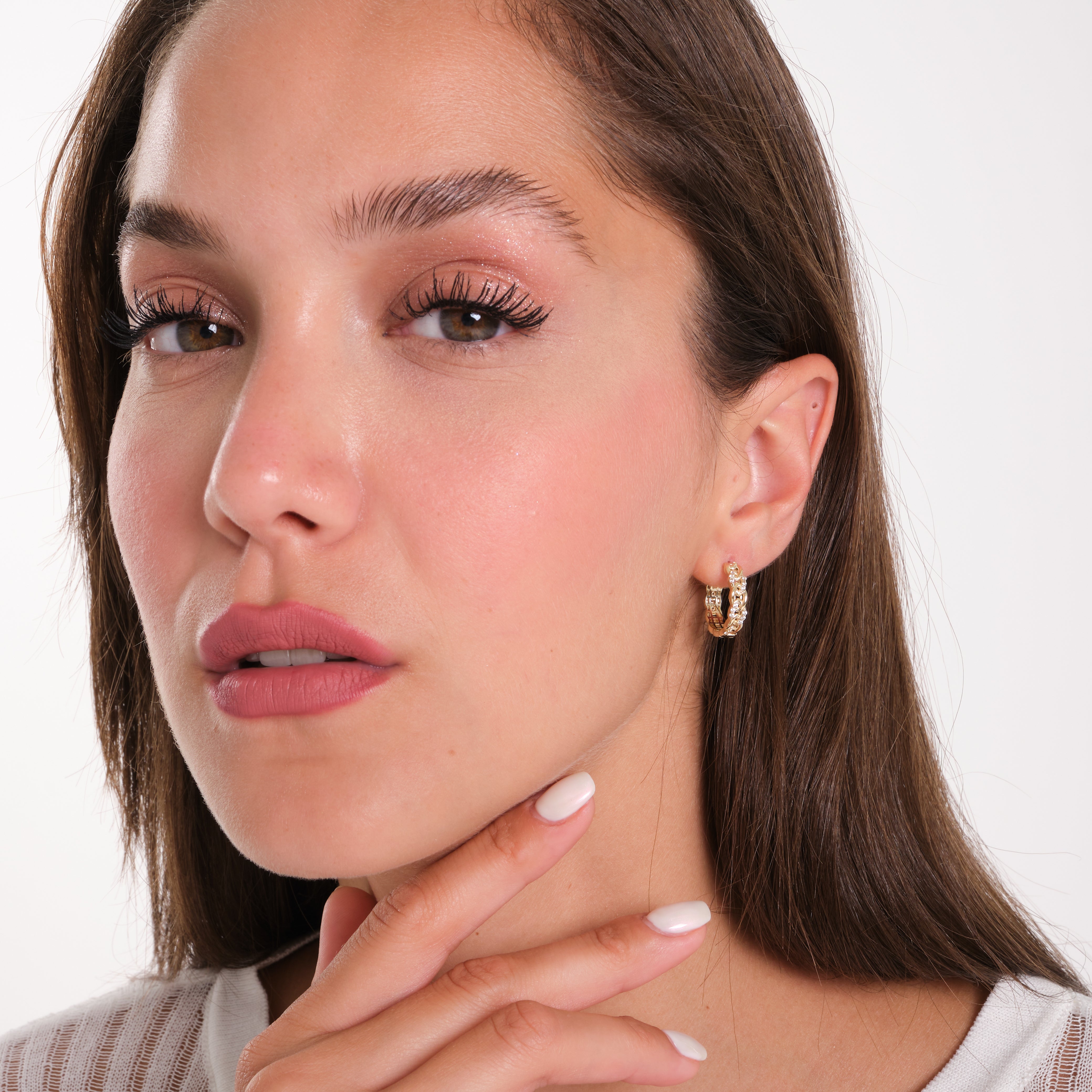 Close-up of a woman wearing gold hoop earrings with a plain background