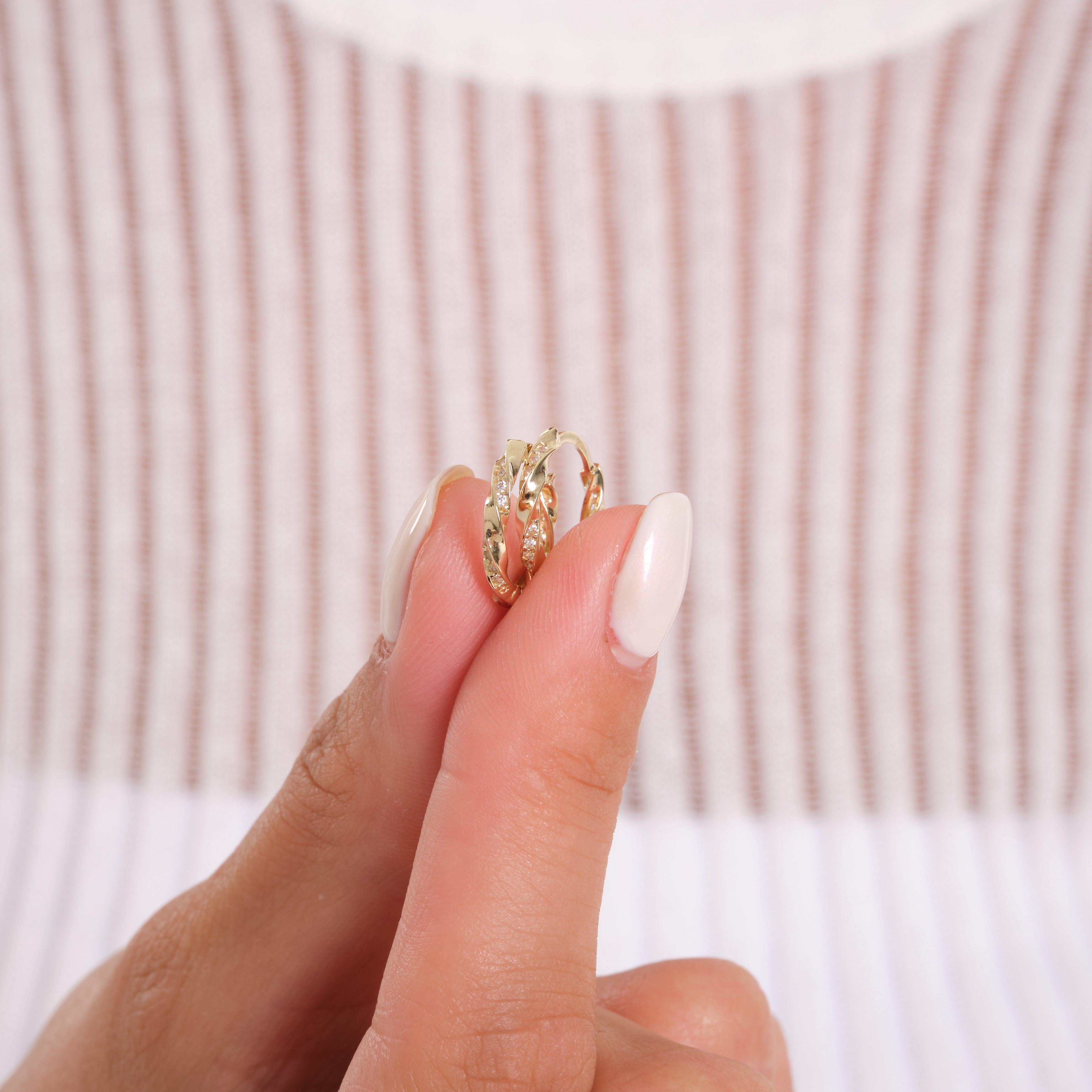 Hand holding gold textured hoop earrings with a striped background