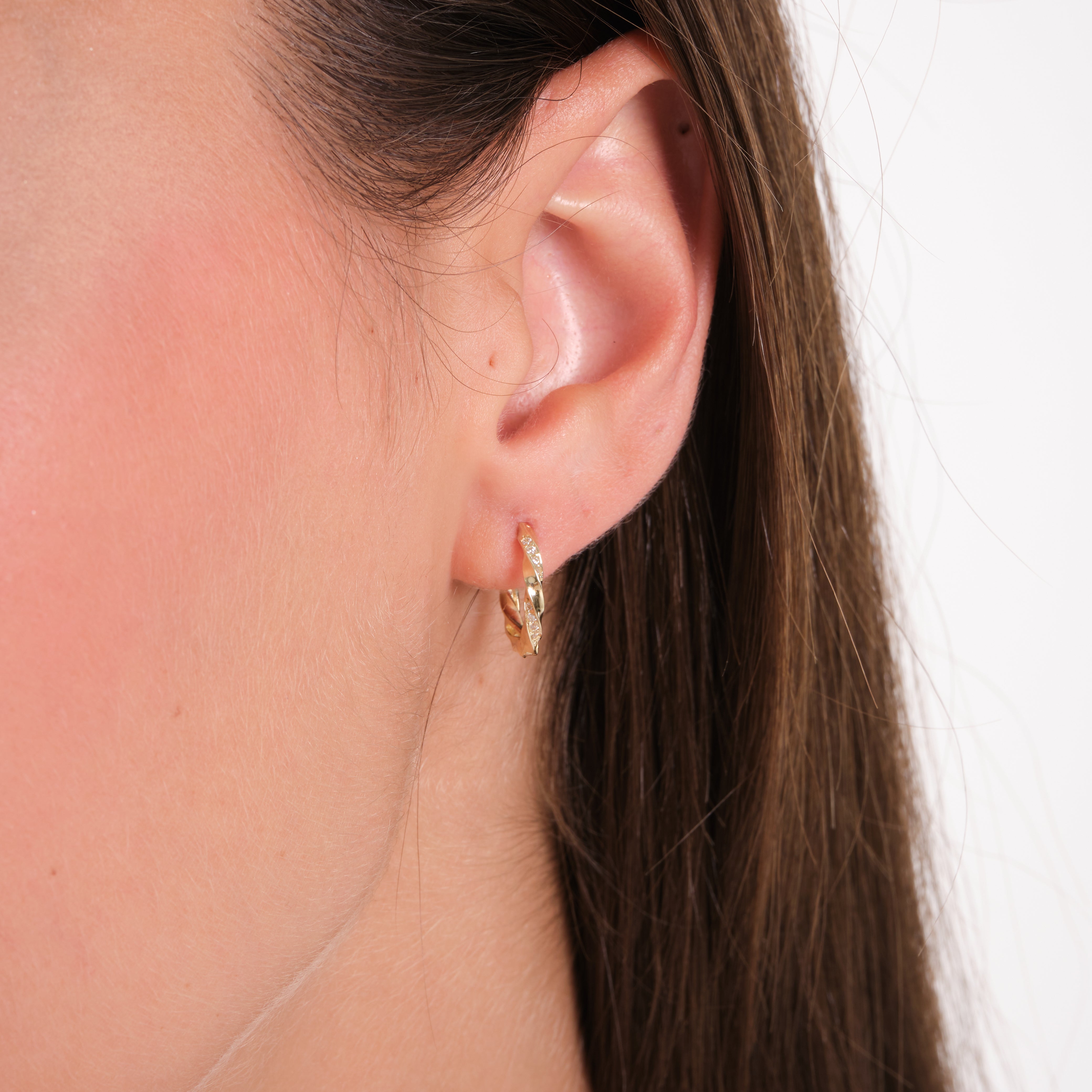 Close-up of an ear wearing a gold earring with a plain background