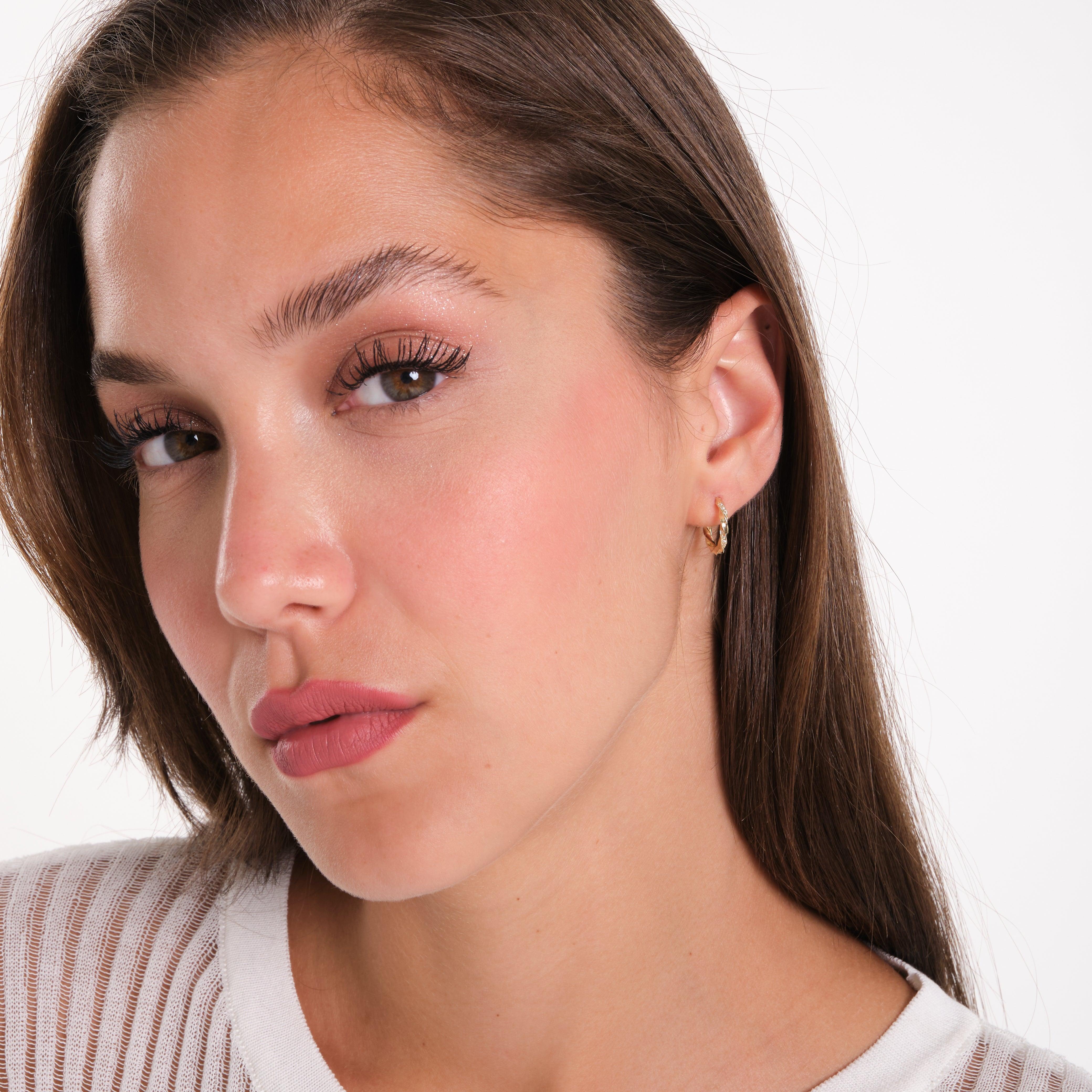 Woman wearing small gold hoop earrings, close-up, with neutral makeup and white top