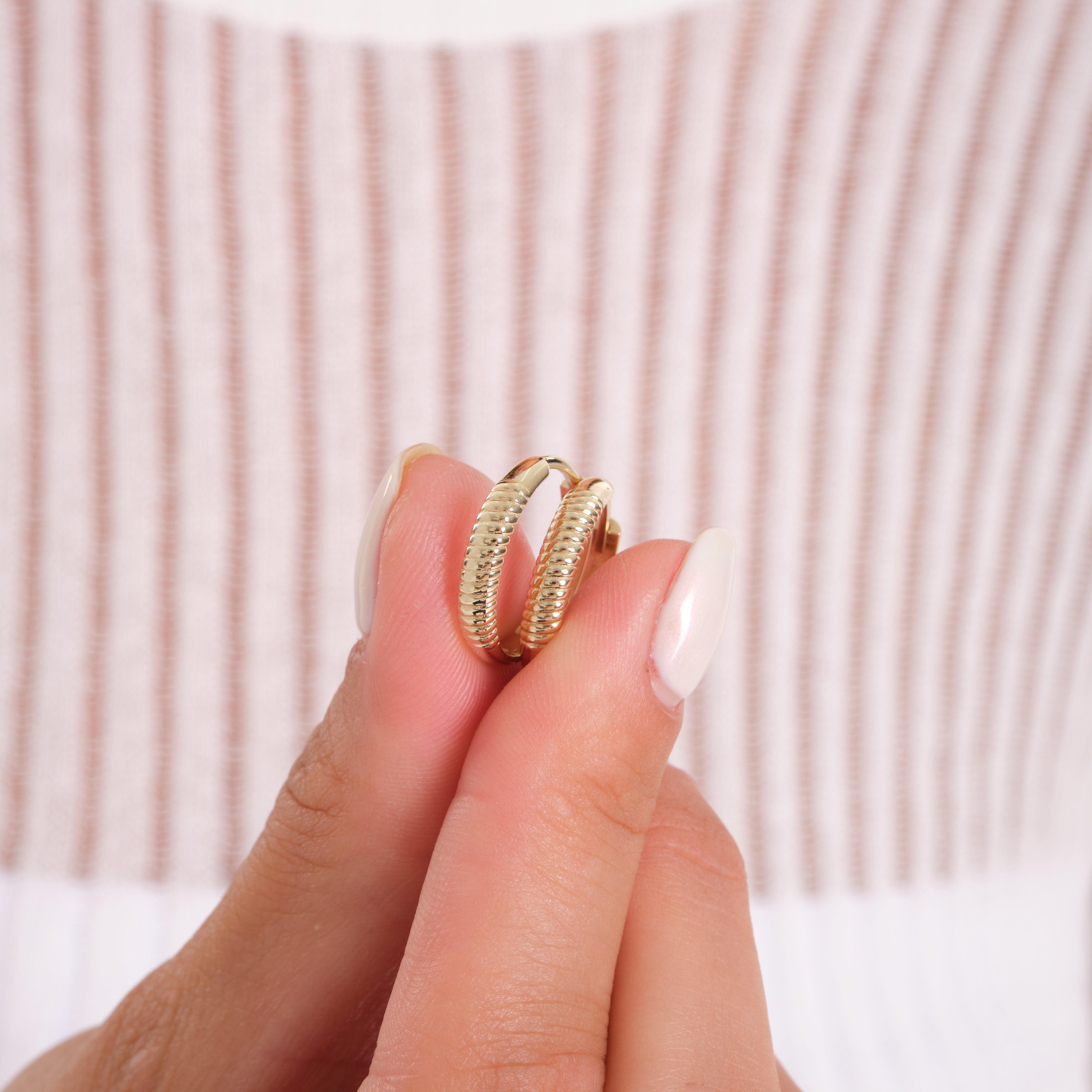 Hand holding textured gold hoop earrings with ribbed design, close-up jewelry photo
