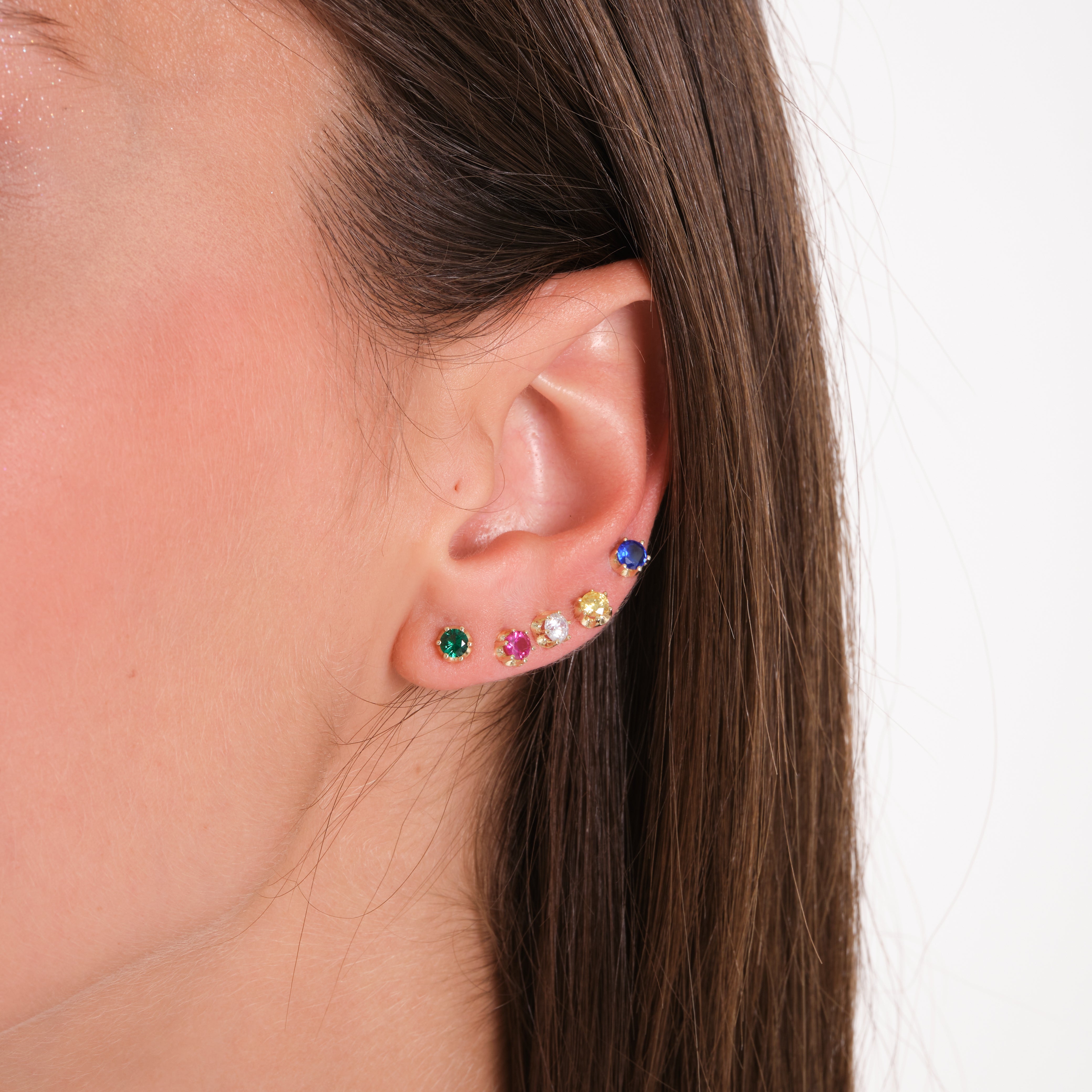 Close-up of an ear wearing colorful stud earrings with a neutral background