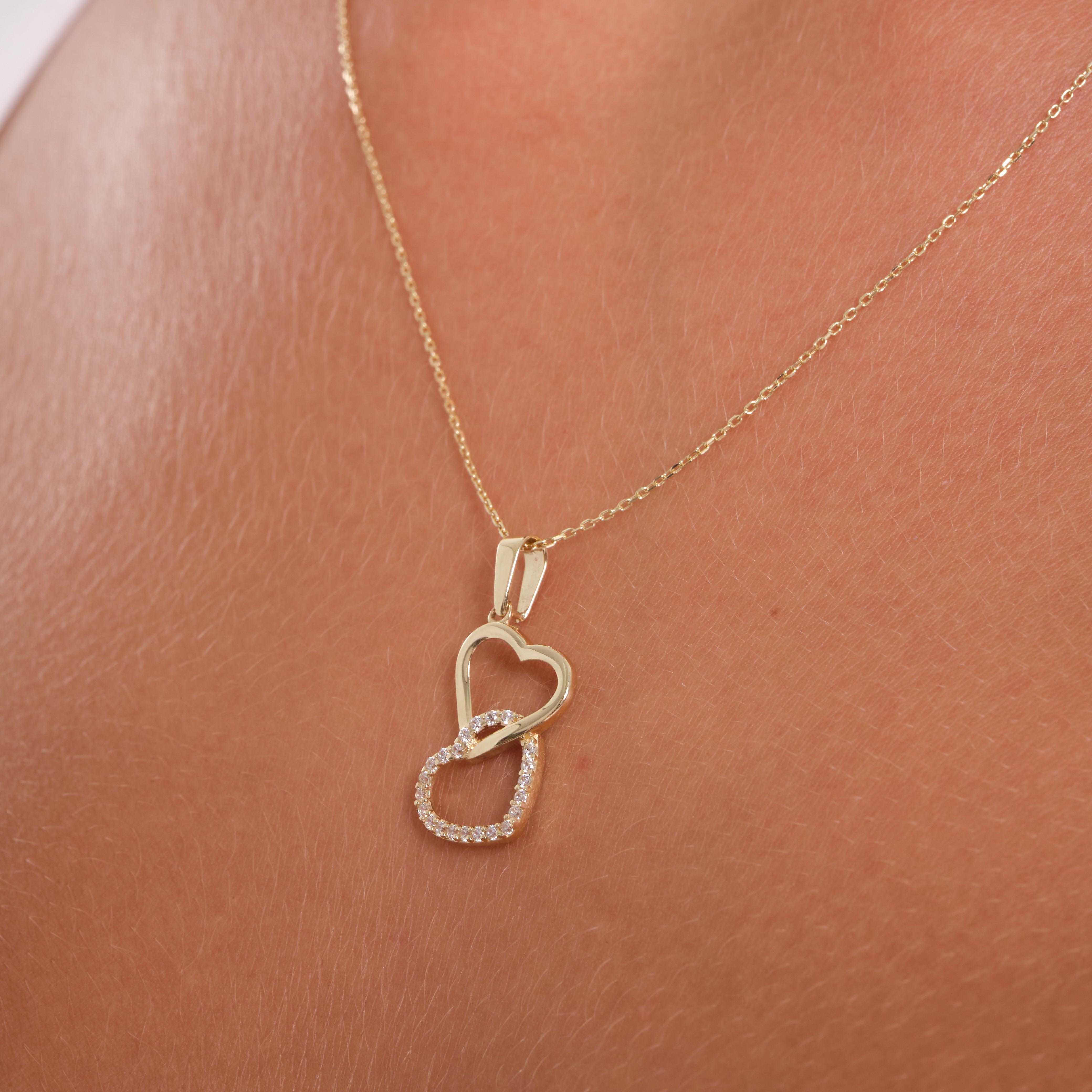 Gold necklace with double heart pendant, one set with small clear stones, on skin close-up