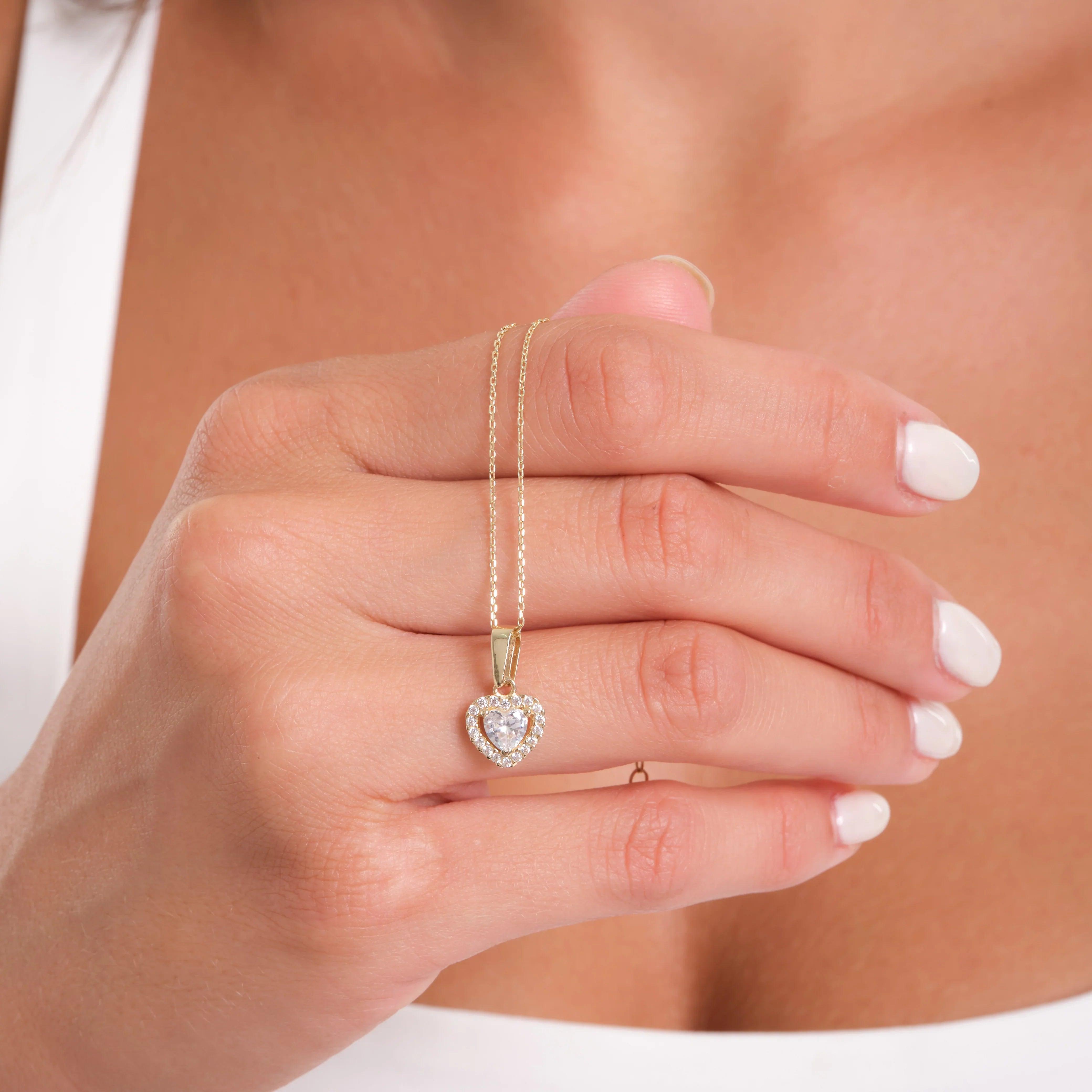 Woman holding gold necklace with heart-shaped diamond pendant