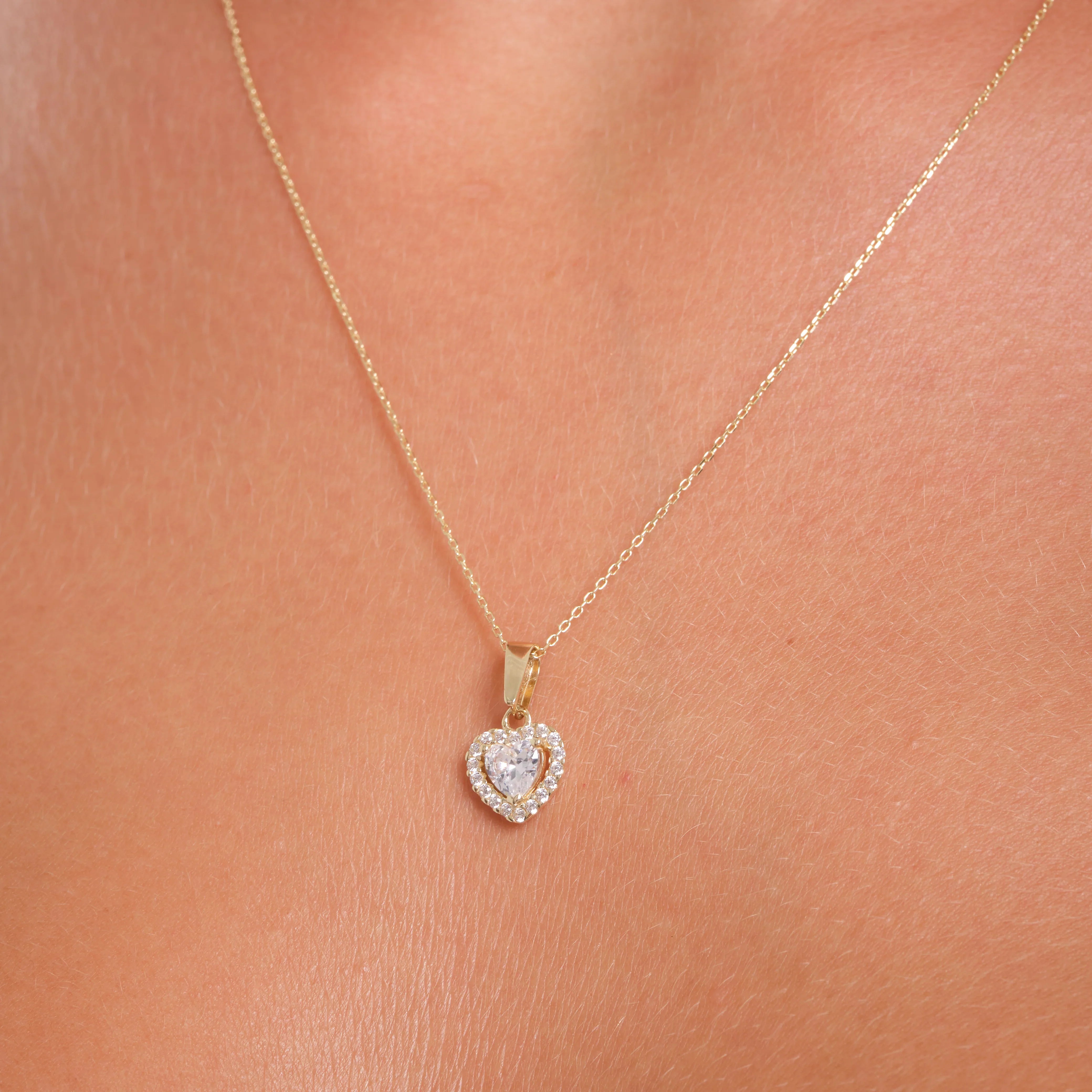 Gold necklace with a heart-shaped pendant on a person's neck