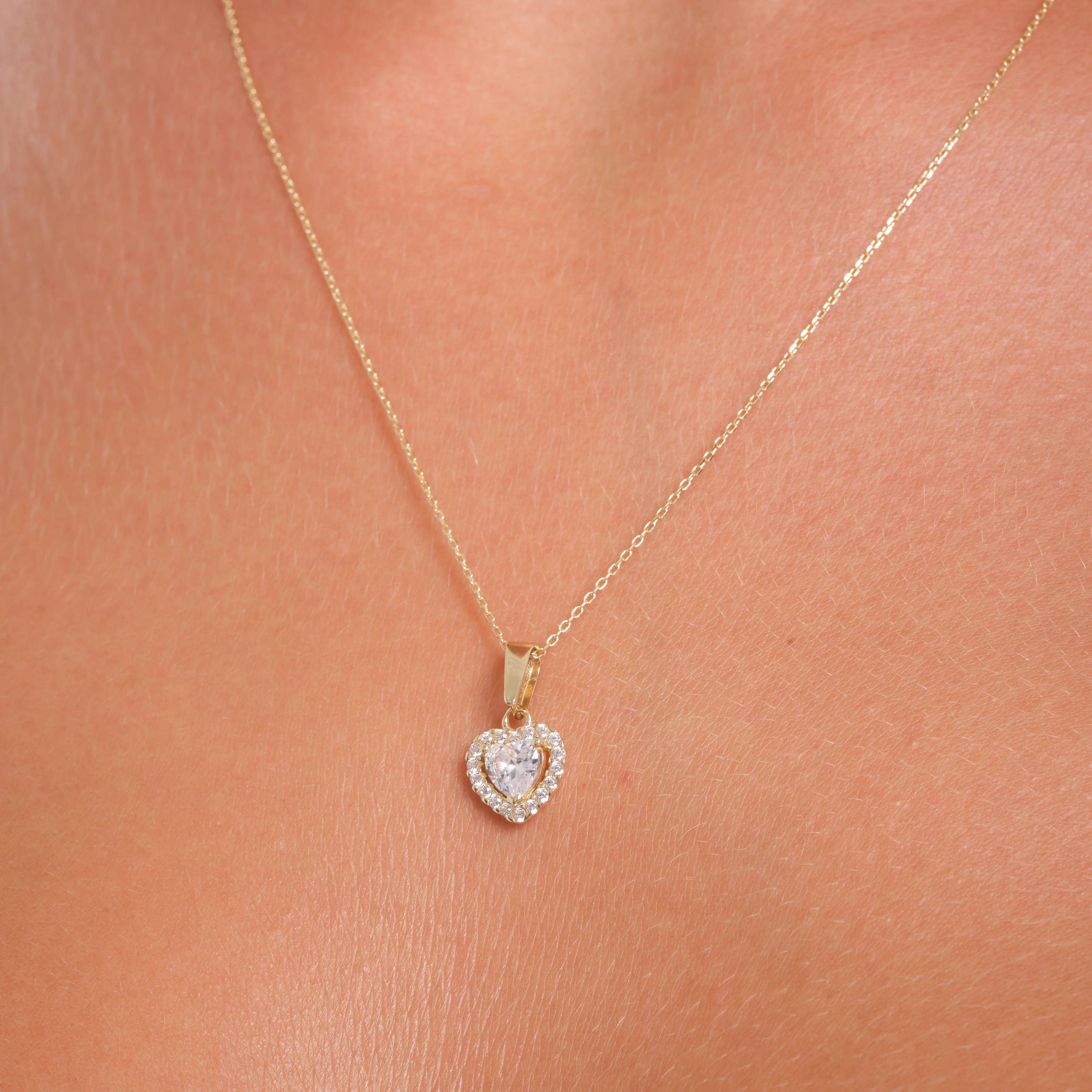 Gold heart-shaped pendant necklace with clear gemstone and diamond accents on skin