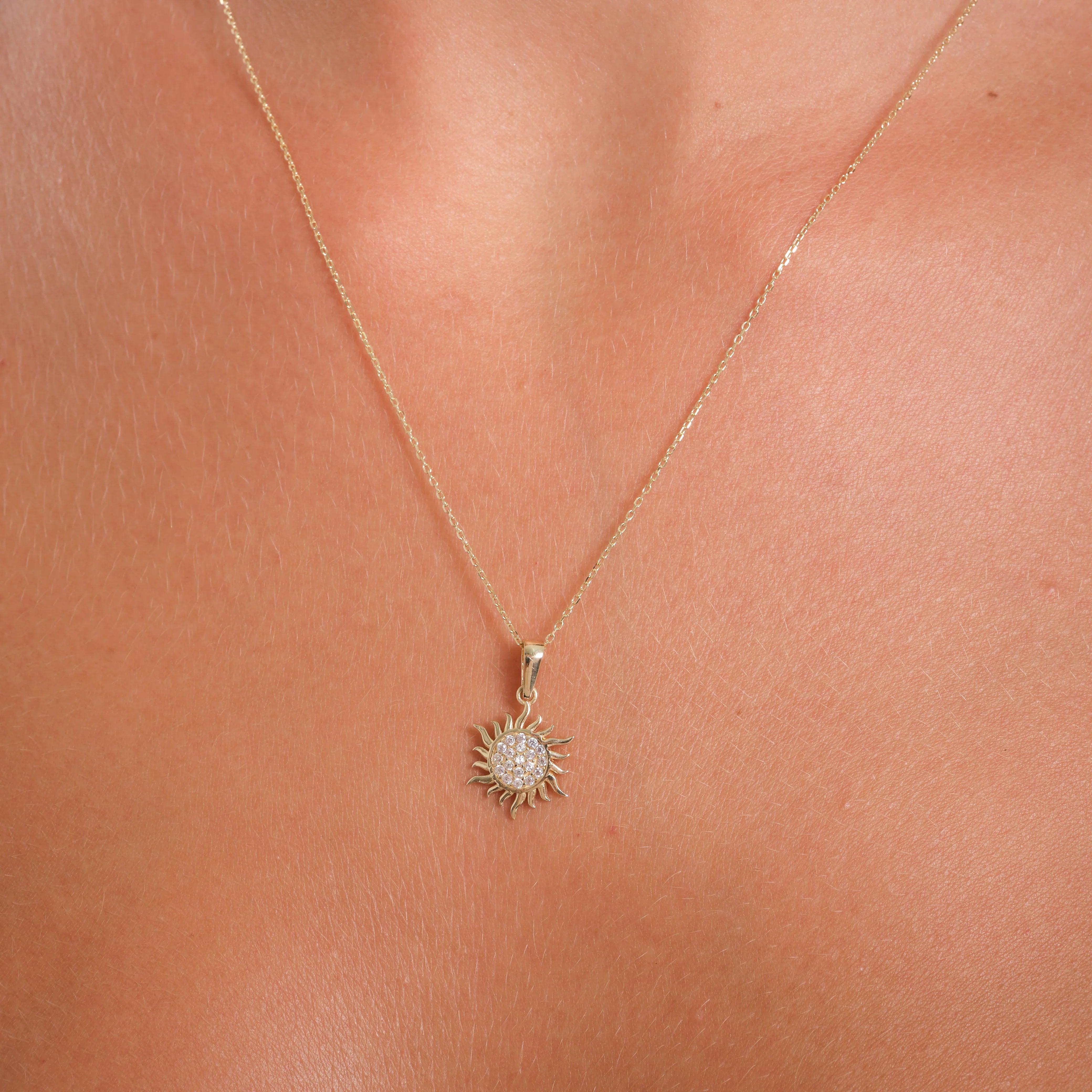 Gold sun pendant necklace with crystal accents on a delicate chain, worn on neck