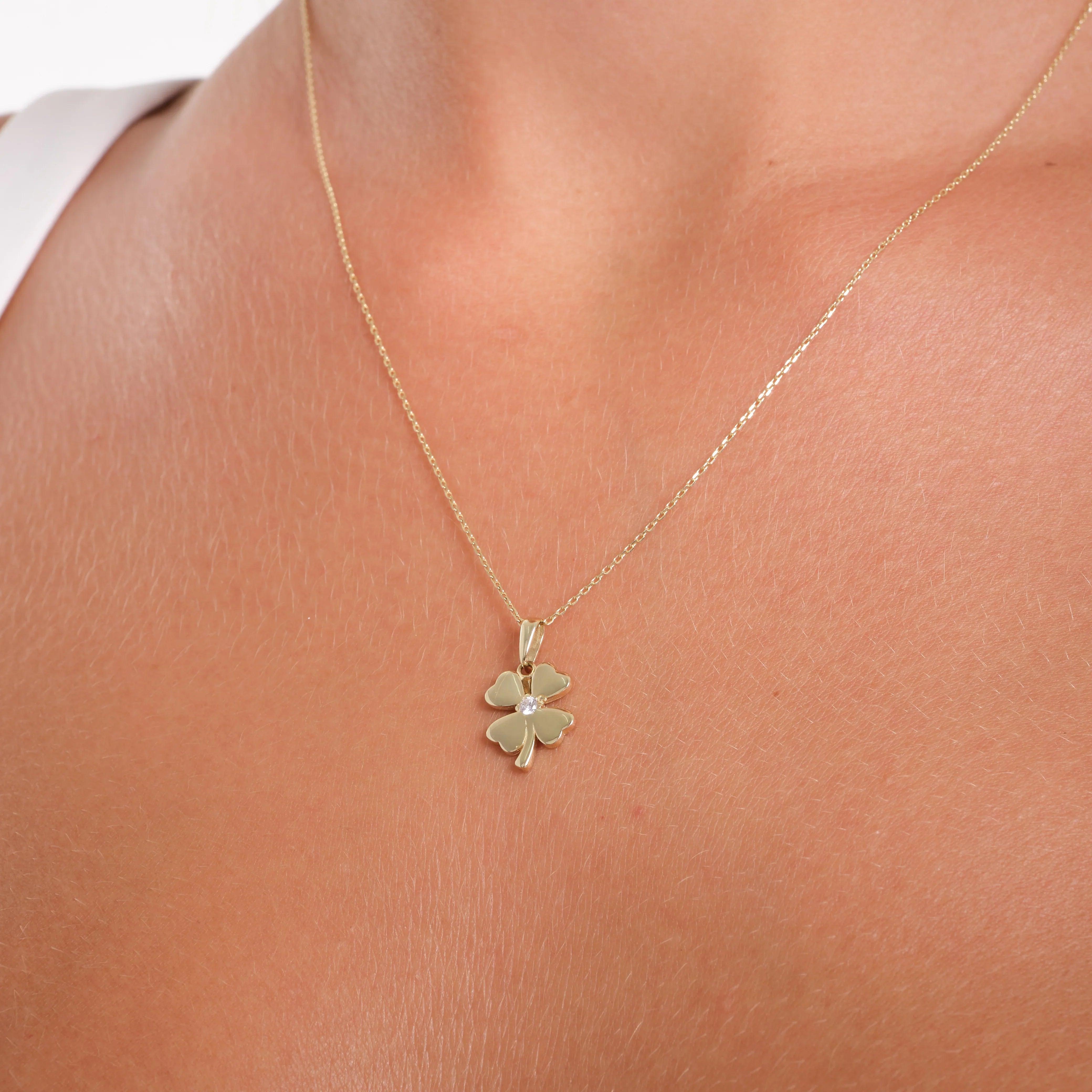 Gold four-leaf clover necklace with gemstone pendant on woman's neck