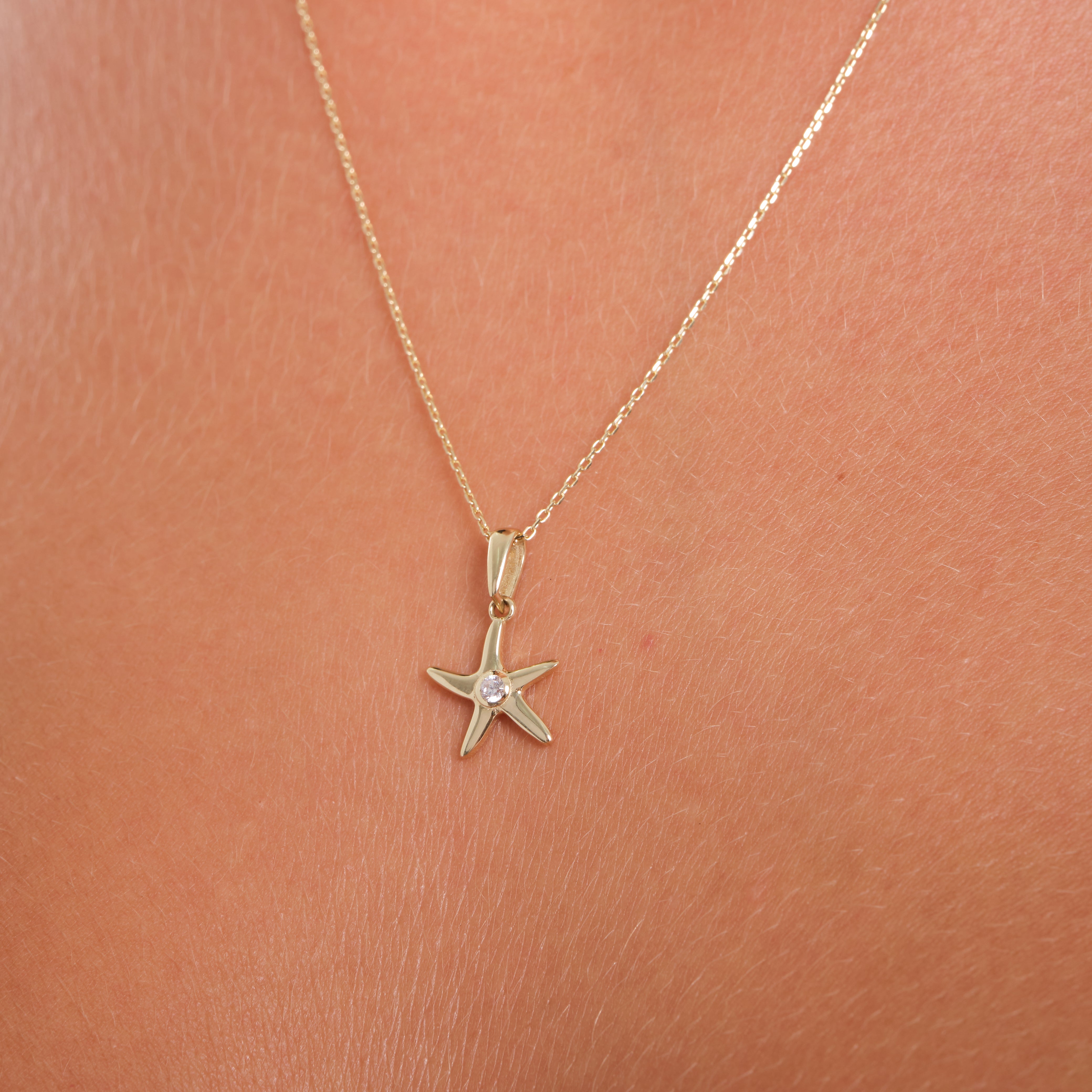 Gold starfish necklace on a person's neck against a pink background