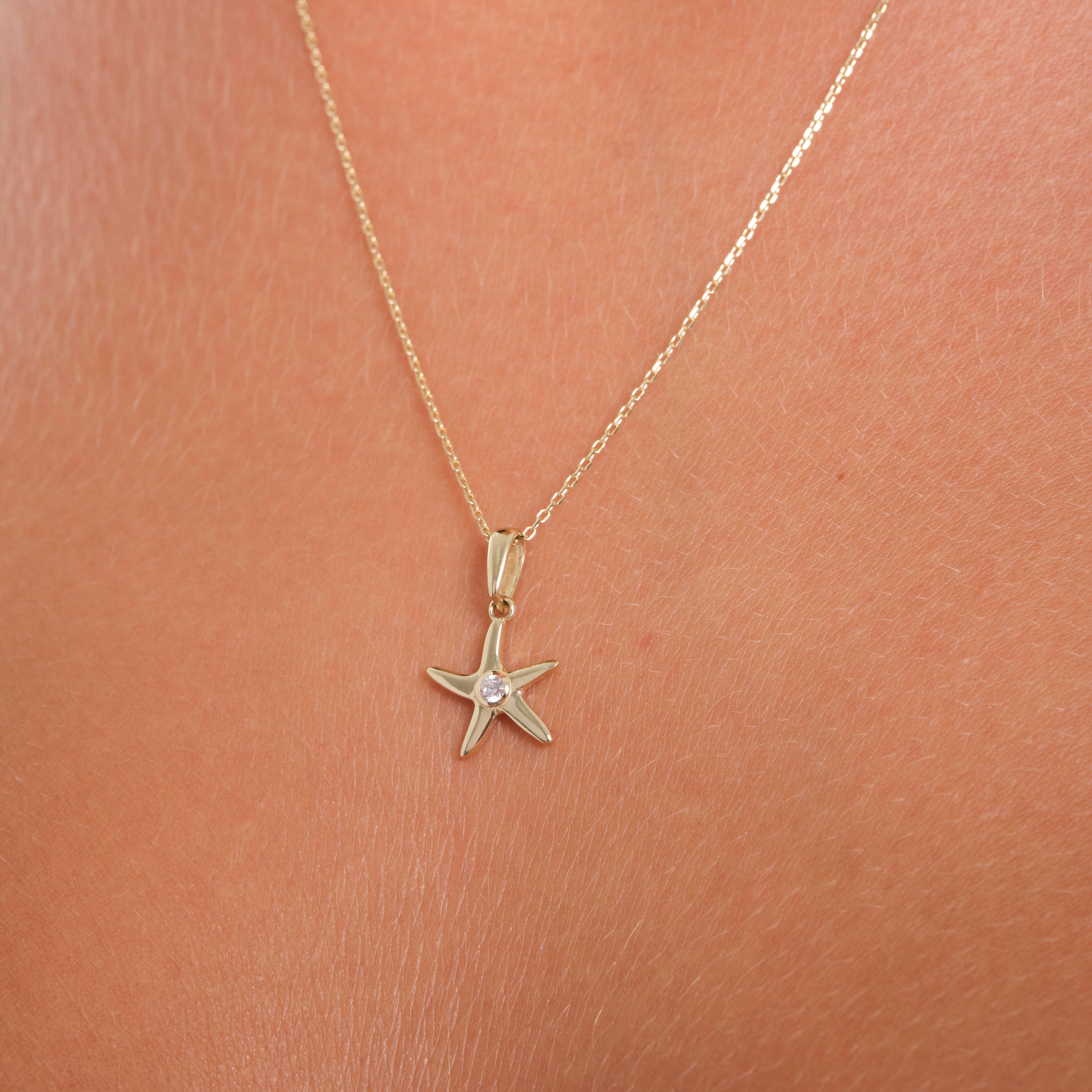 Gold starfish pendant necklace with clear gemstone center on skin