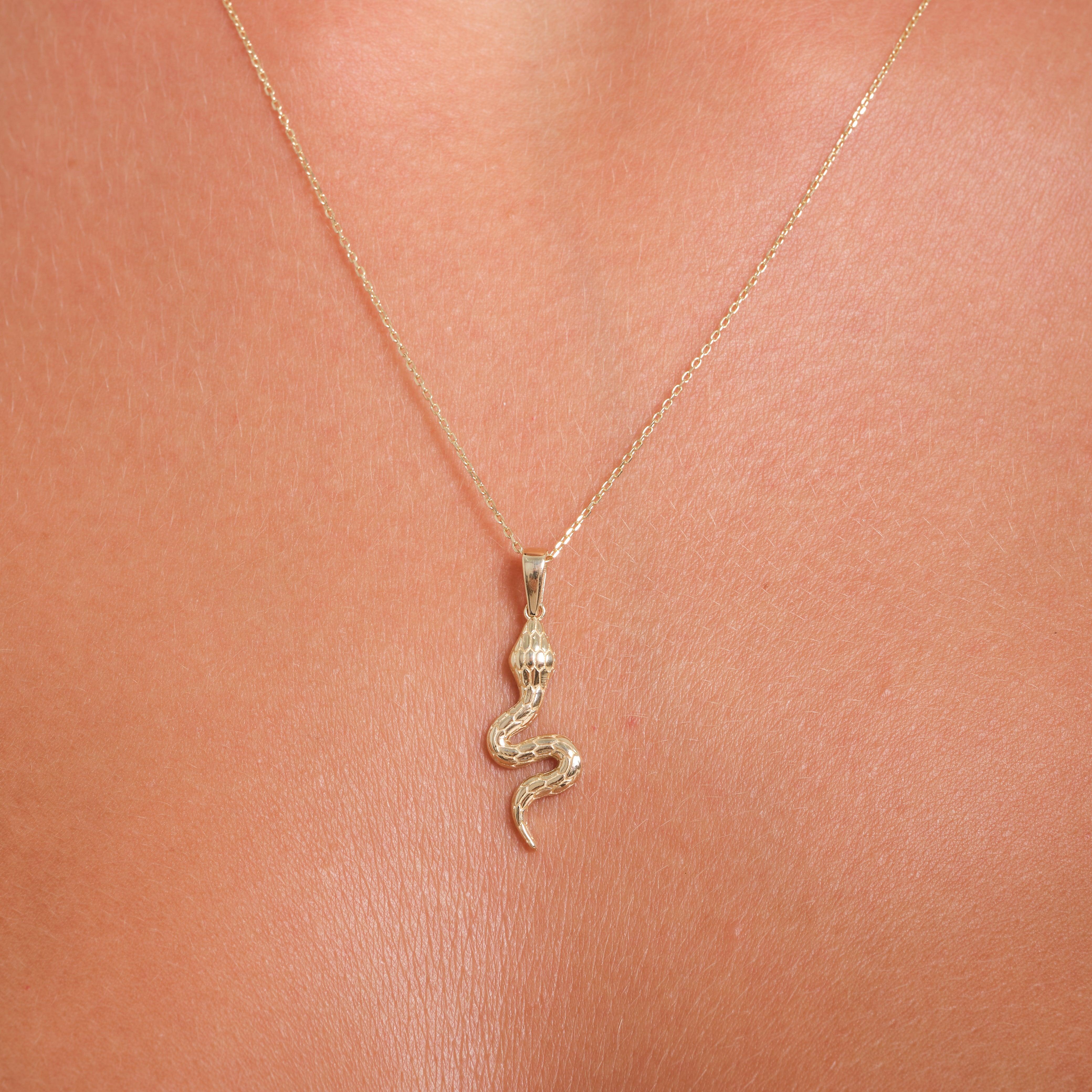Gold snake pendant necklace on skin, delicate chain, fine jewelry close-up