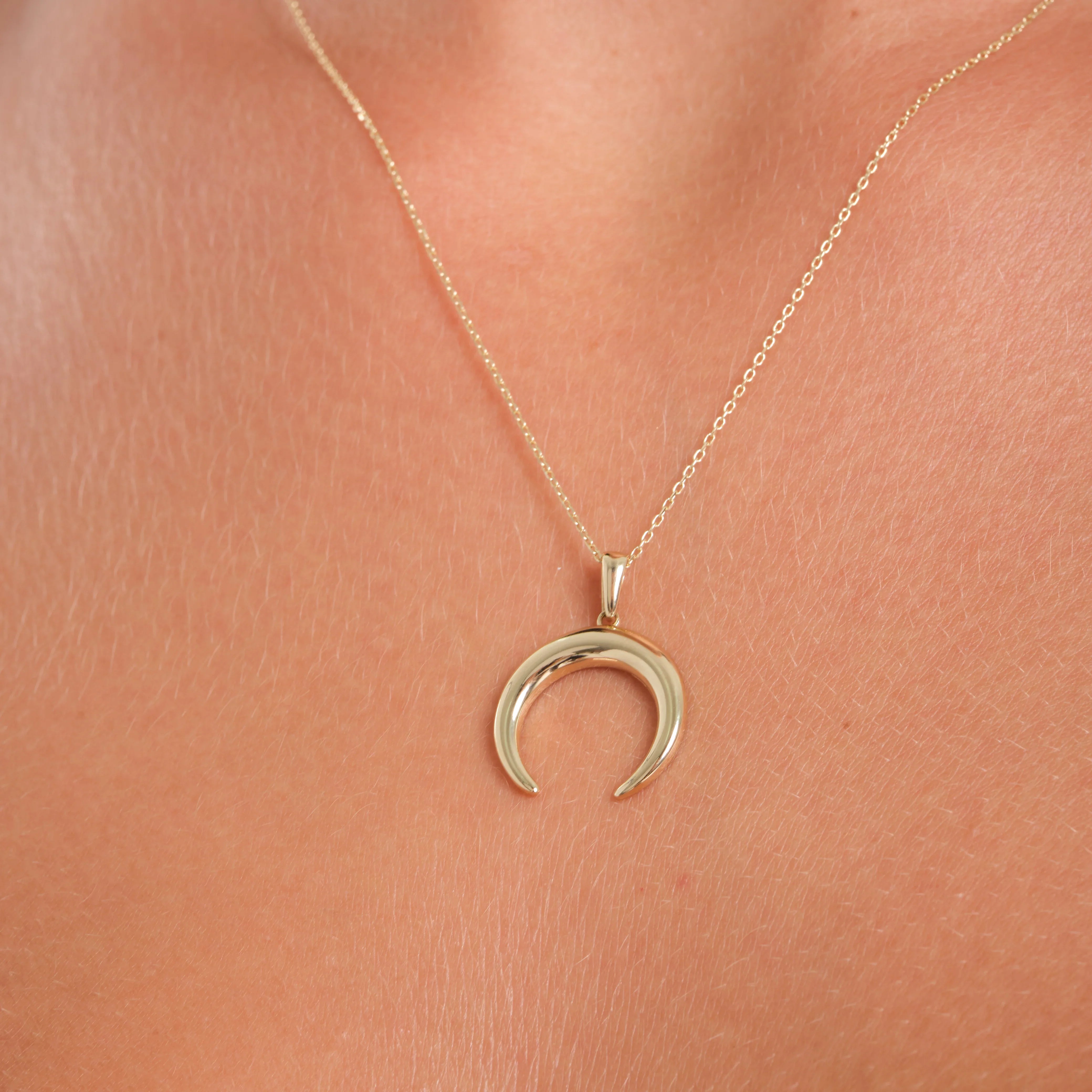 Gold crescent moon necklace on a person's neck against a pink background