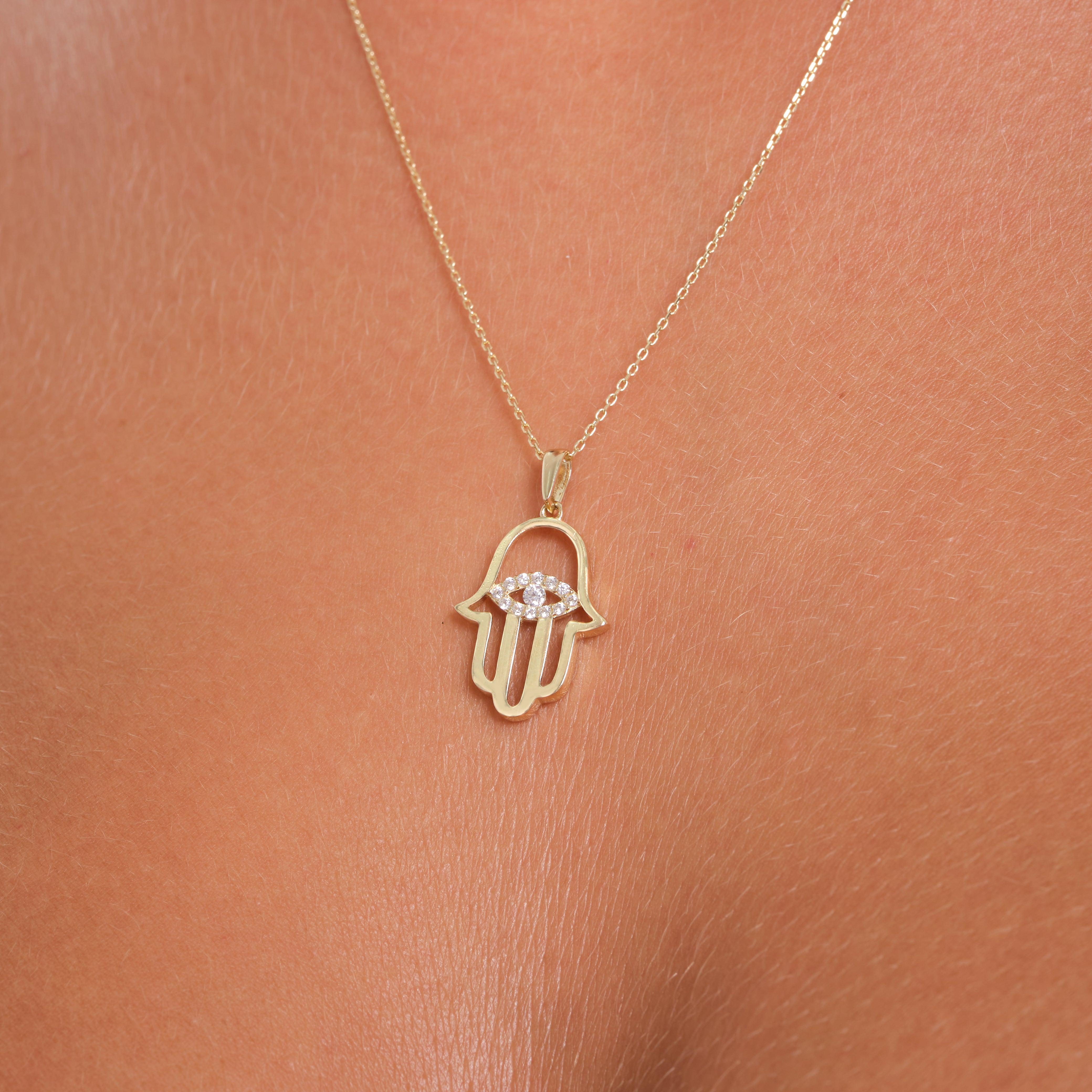 Gold hamsa hand pendant necklace with diamond accents on model's neck