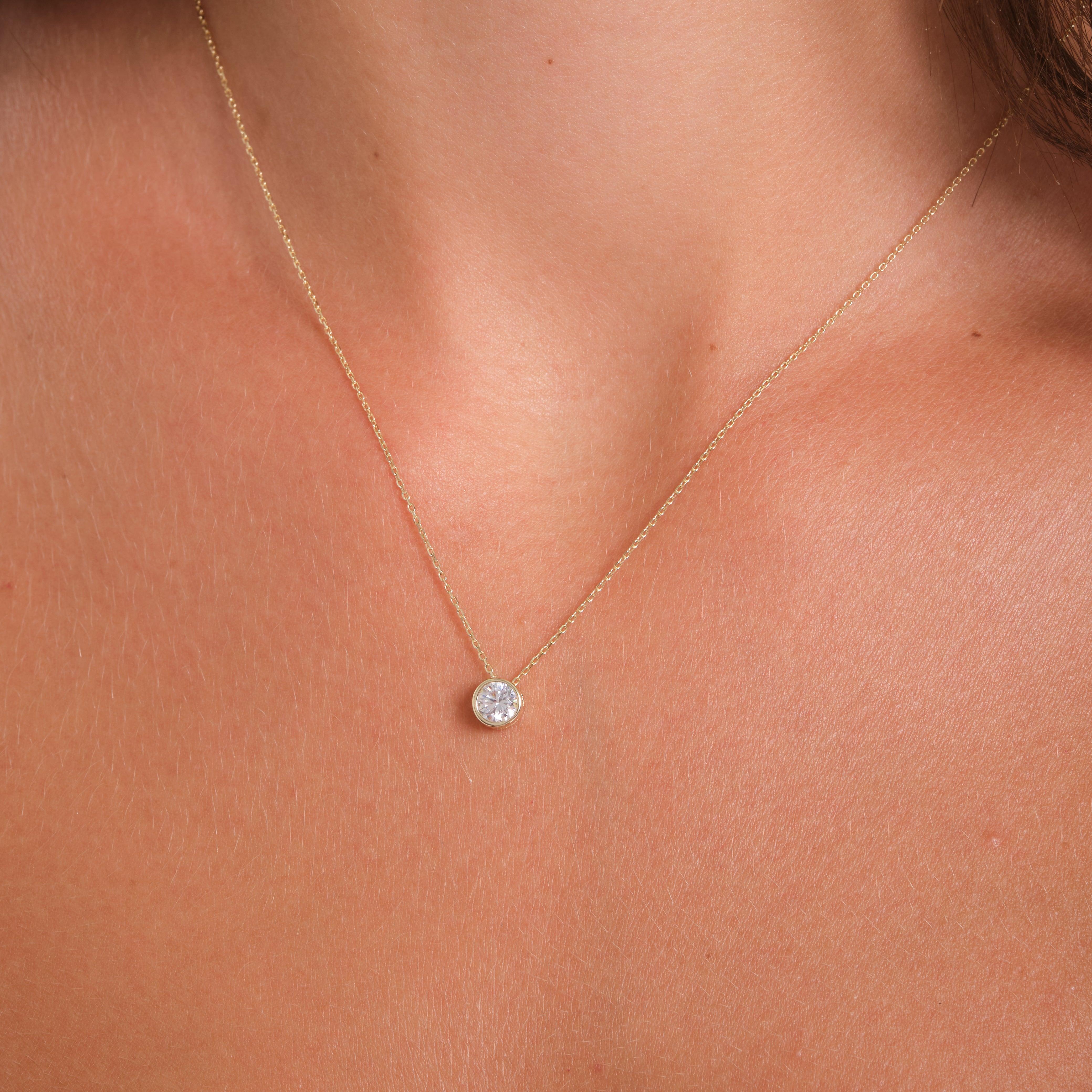 Gold necklace with round solitaire diamond pendant on woman's neck
