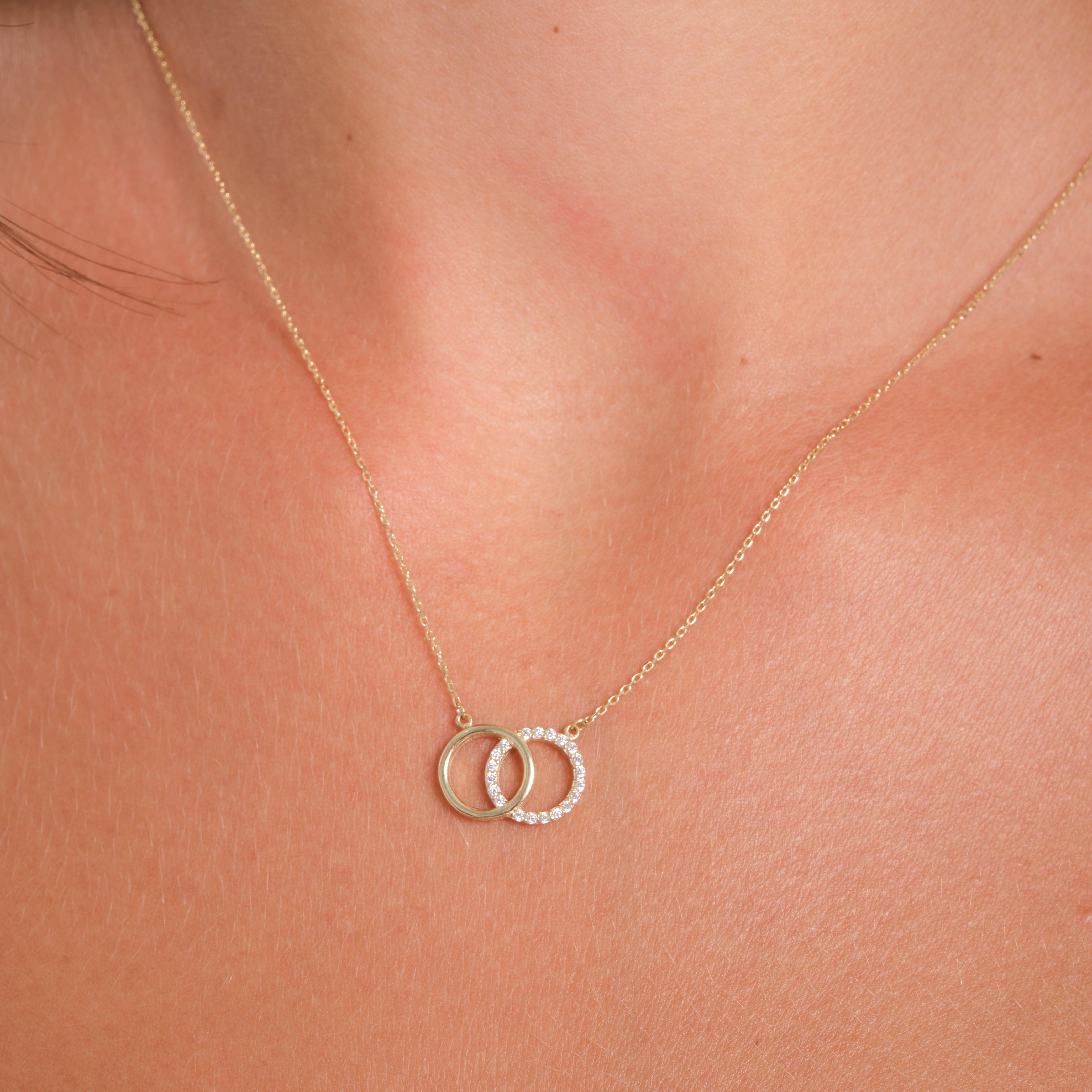 Gold necklace with interlocking rings, one set with small clear stones, on a woman's neck