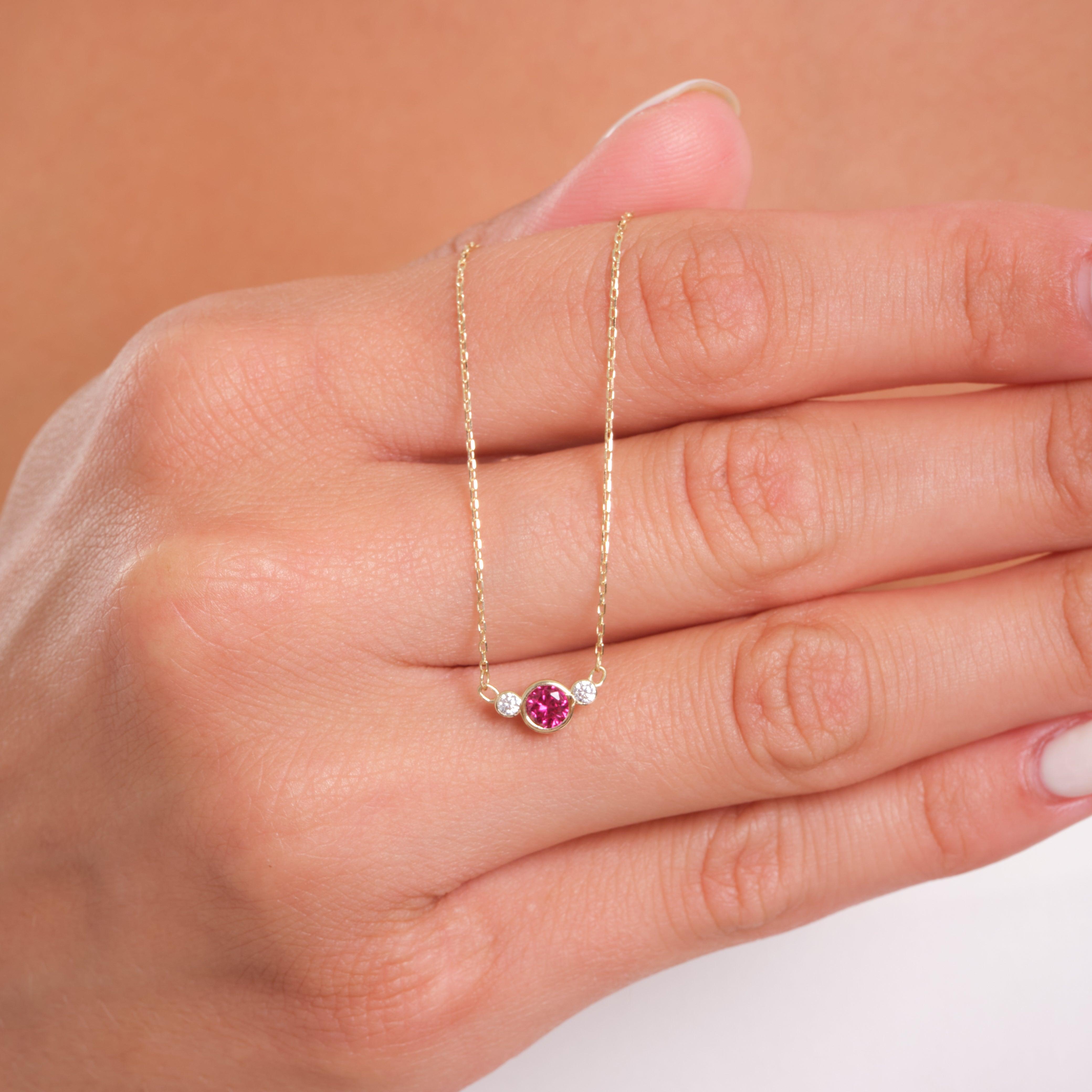 Delicate gold necklace with pink gemstone and diamonds held on a woman's hand