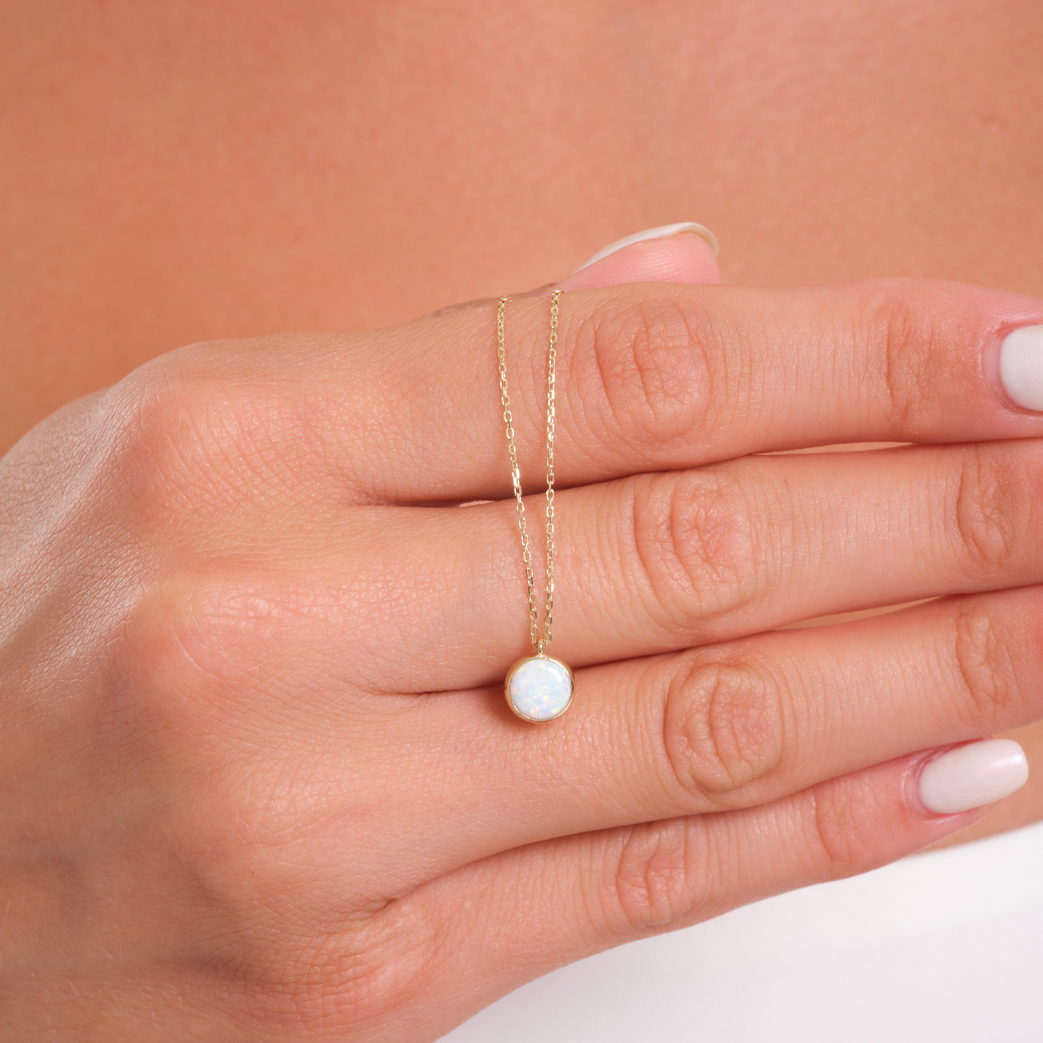 Gold chain necklace with round opal pendant displayed on woman's hand