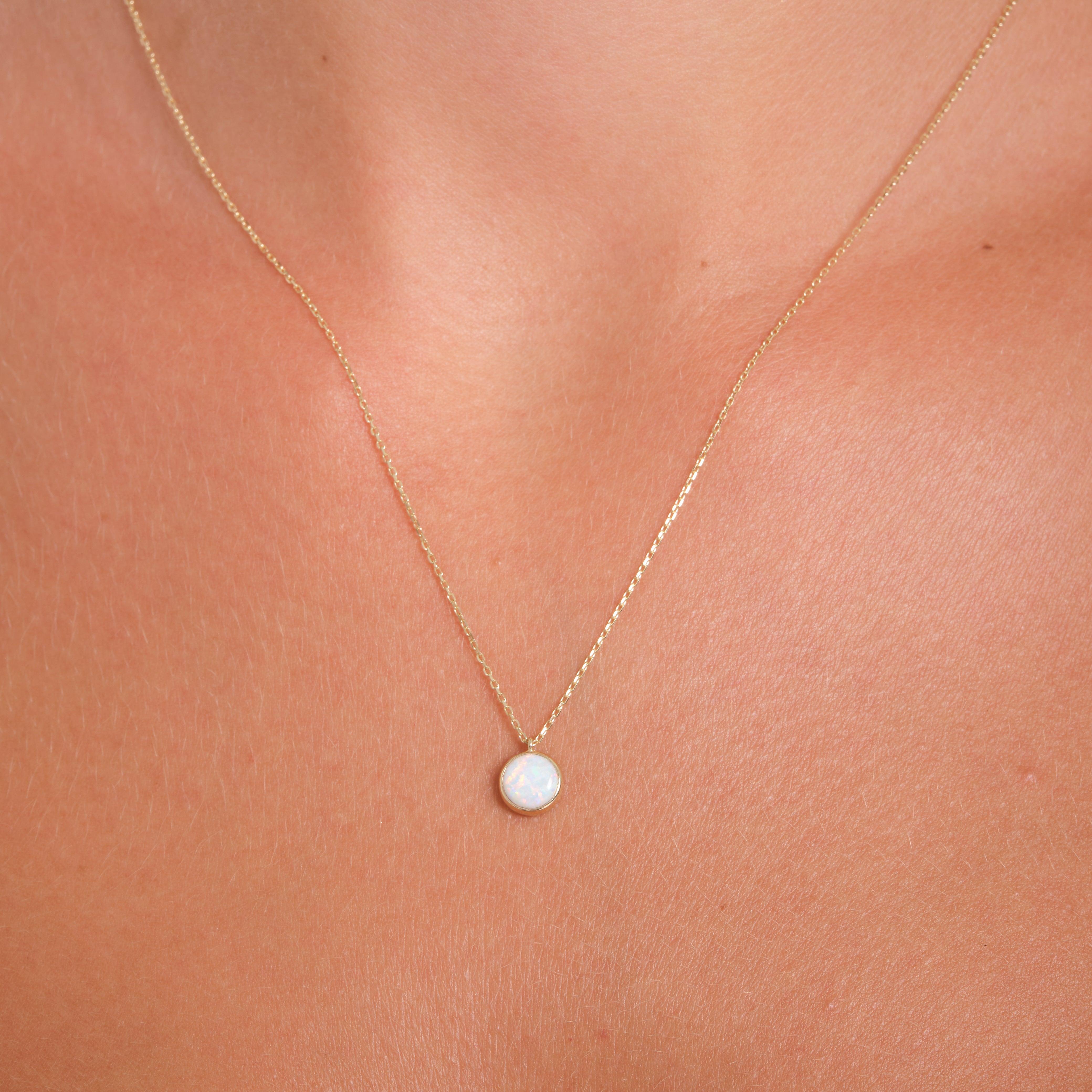 Delicate gold chain necklace with a round opal pendant on a woman's neck