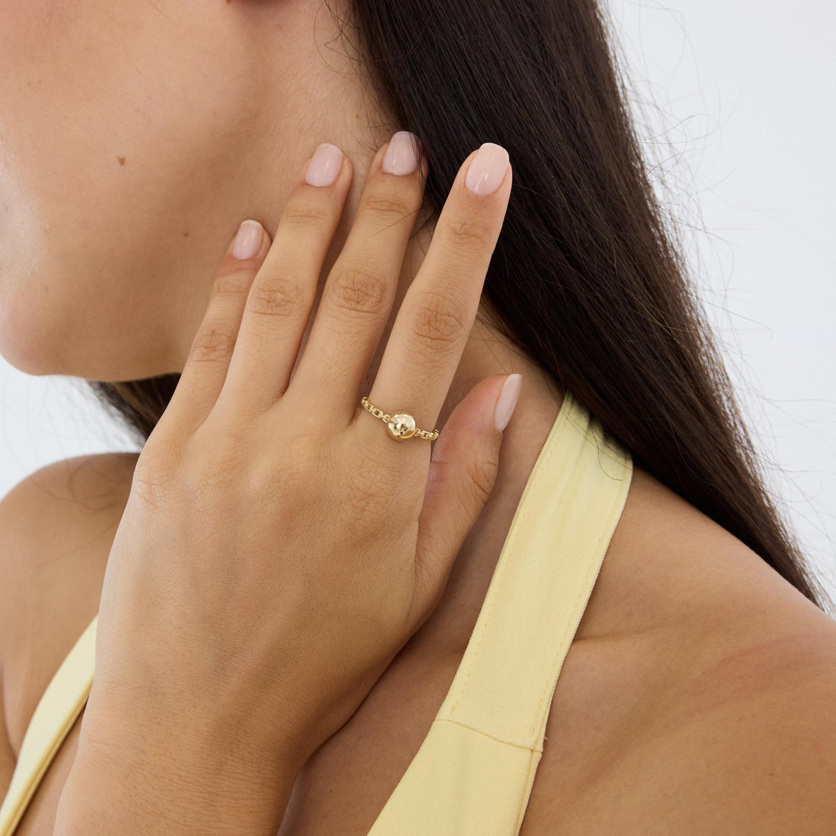 14K yellow gold ball ring worn on a hand held against the neck, model in side profile
