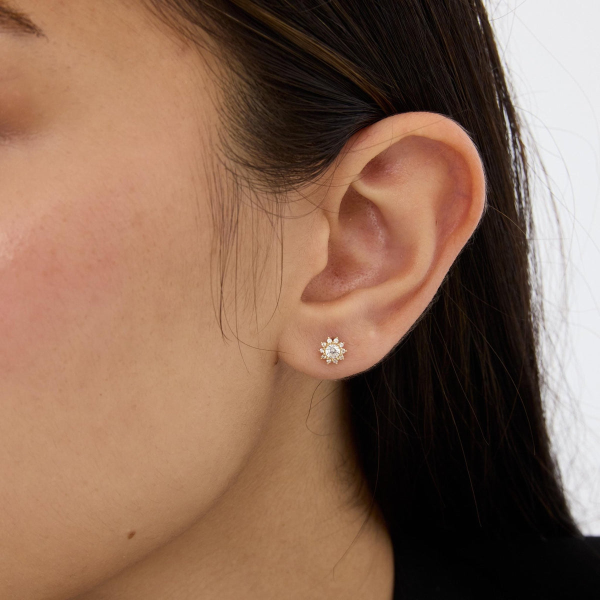 14K gold cubic zirconia halo stud worn on a pierced earlobe, close-up with dark hair behind