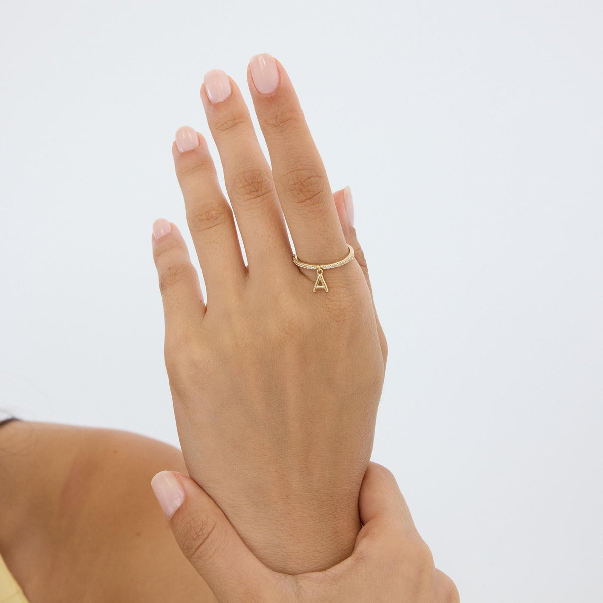 14K yellow gold dangle initial ring worn on a raised hand, back of the hand toward the camera