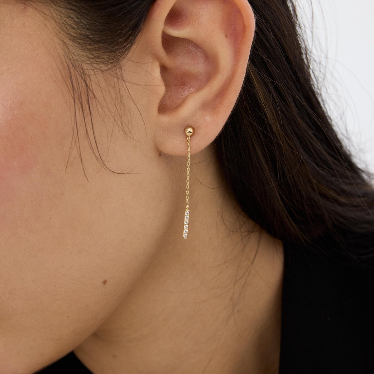 14K gold drop stud earring with round cubic zirconia bar worn on ear, close-up side profile