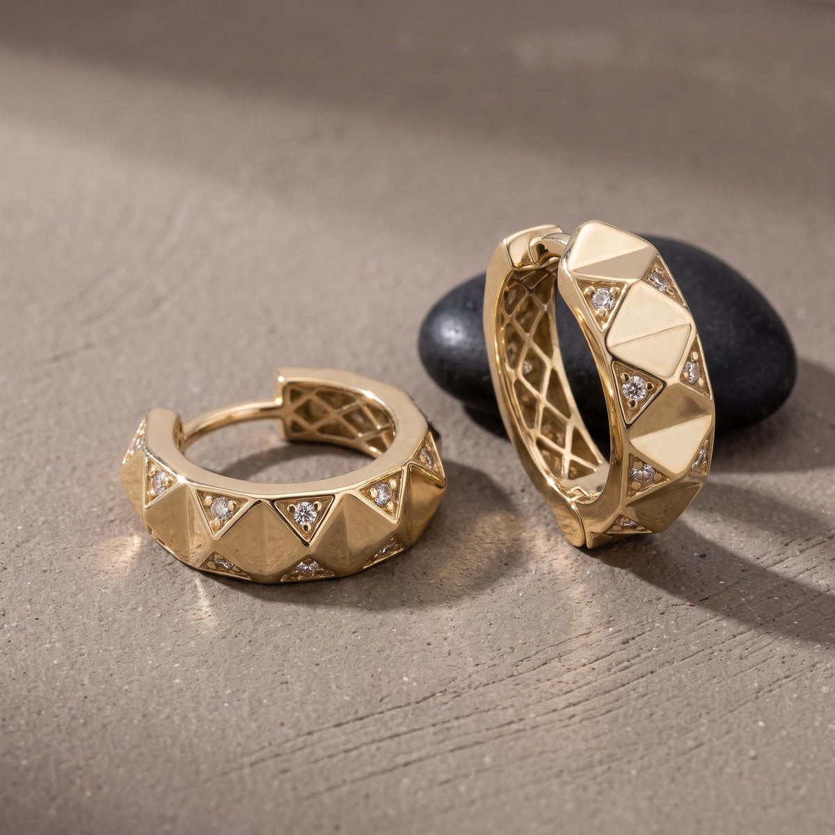14K yellow gold geometric huggie earrings with cubic zirconia, pair resting on a dark stone
