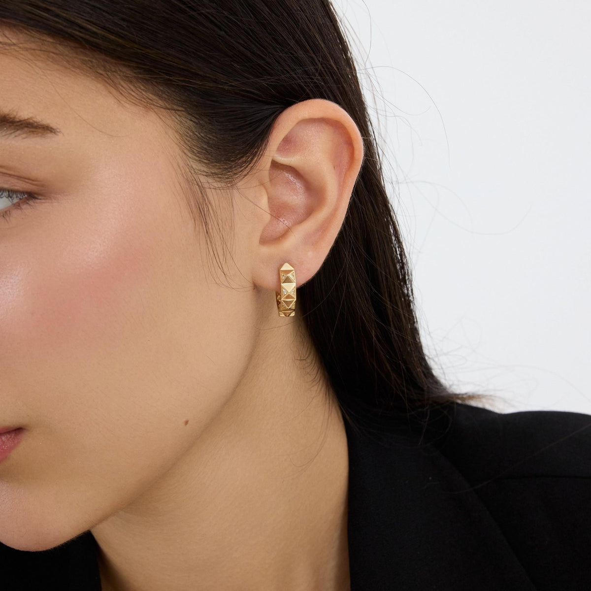 14K gold geometric huggie earring worn in the ear, woman in profile with black blazer