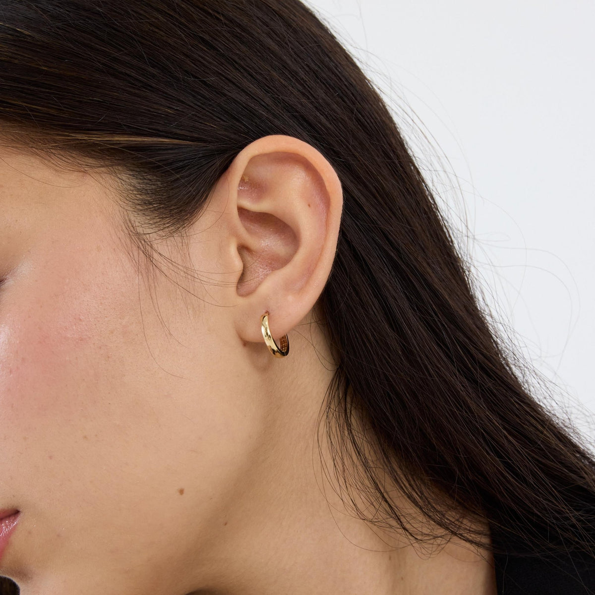 14K gold huggie hoop earring worn on the ear, angled view with hair swept back