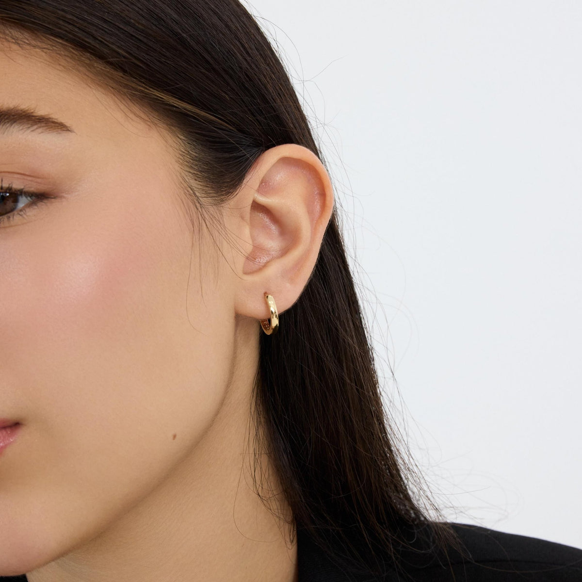14K gold huggie hoop earring worn on the ear, front-facing view with black collar