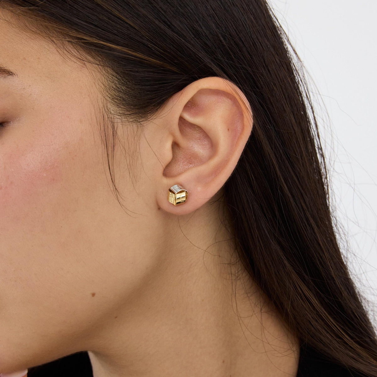 14K gold knot stud earring worn on ear, model with long dark hair, profile view