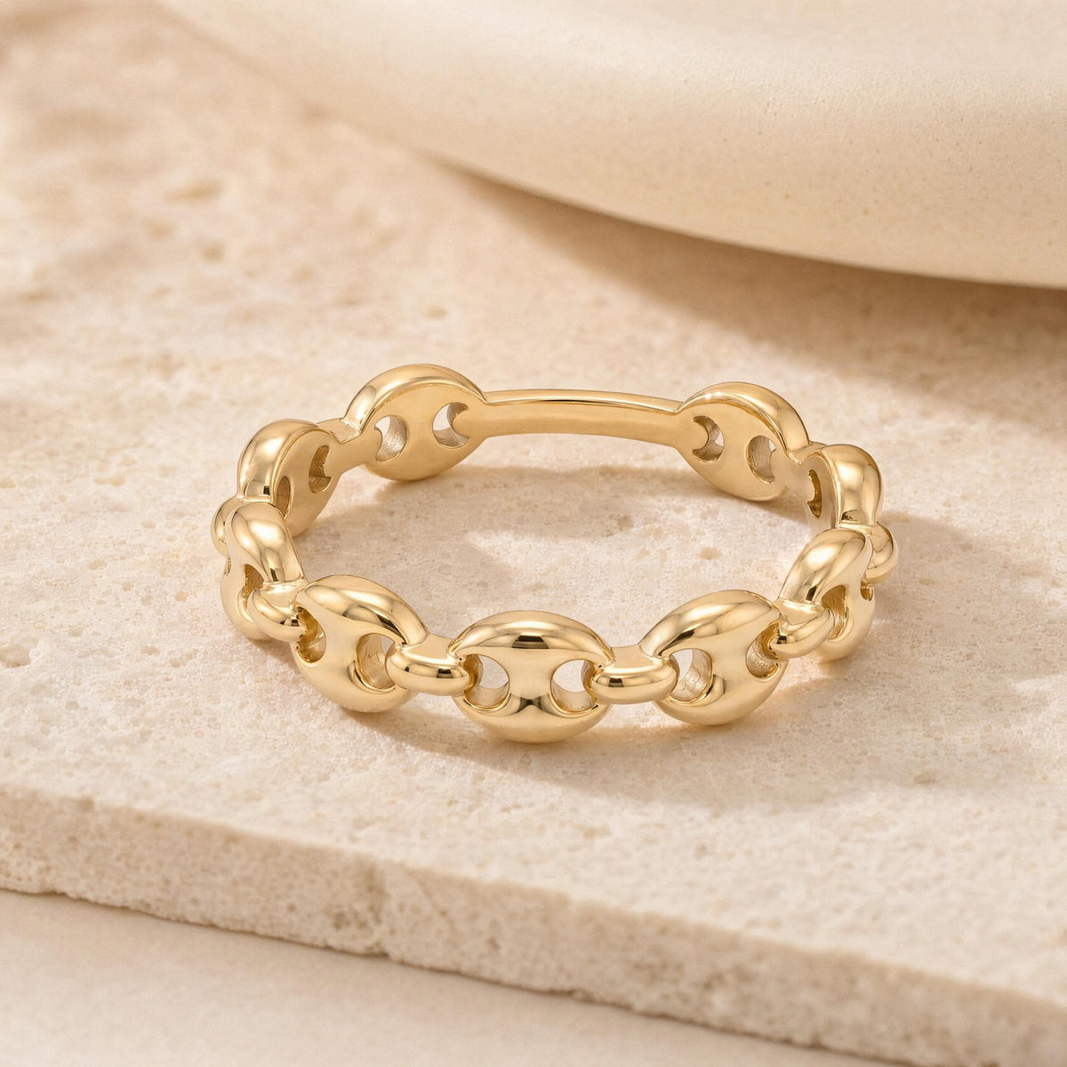 14K gold mariner link ring standing upright on textured stone surface