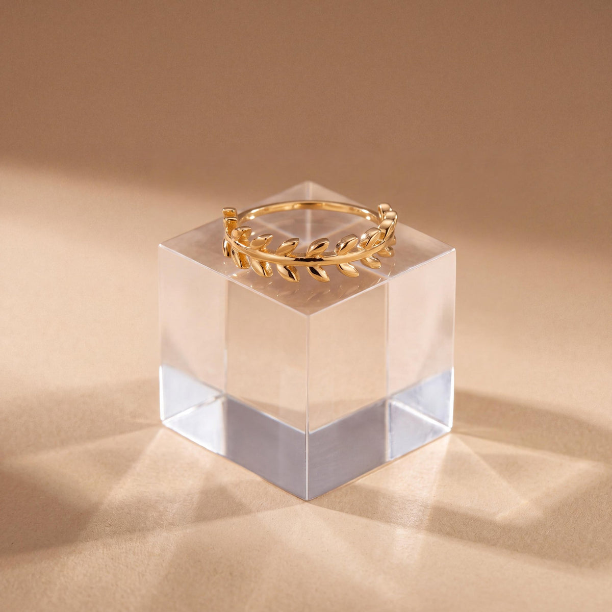 14K yellow gold olive leaf ring displayed on a clear acrylic cube against a warm beige backdrop