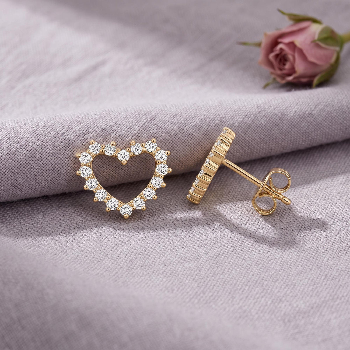 14K gold open heart stud earrings with round cubic zirconia, front and side view on lilac linen beside a rose