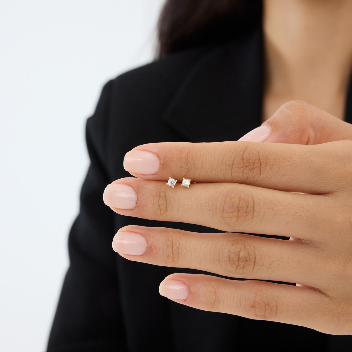 Pair of 14K gold round cubic zirconia solitaire studs shown on a fingertip to show their tiny size