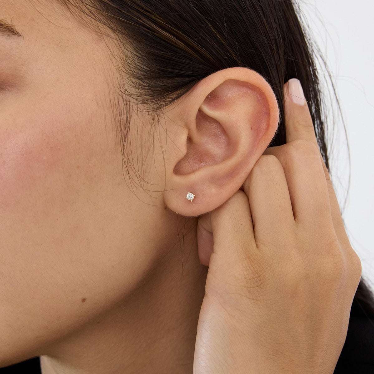 14K gold round cubic zirconia solitaire stud earring worn in the ear, hand touching behind the ear