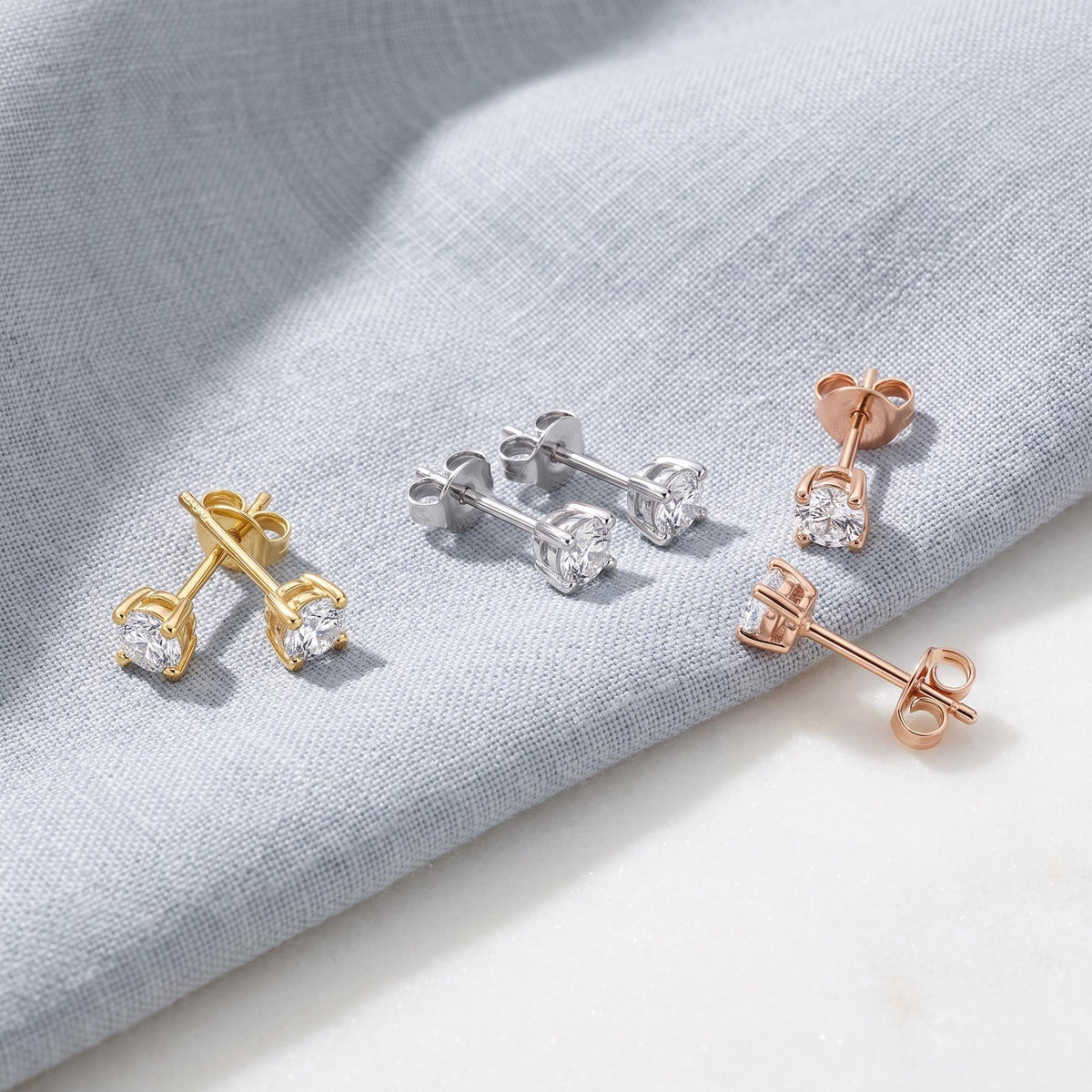 14K round cubic zirconia solitaire stud earrings in yellow, white and rose gold, three pairs on grey linen