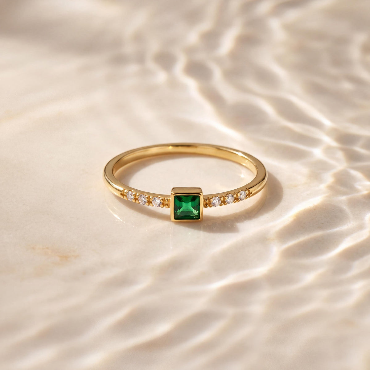 14K yellow gold square simulated emerald ring lying on a pale surface under rippling water light