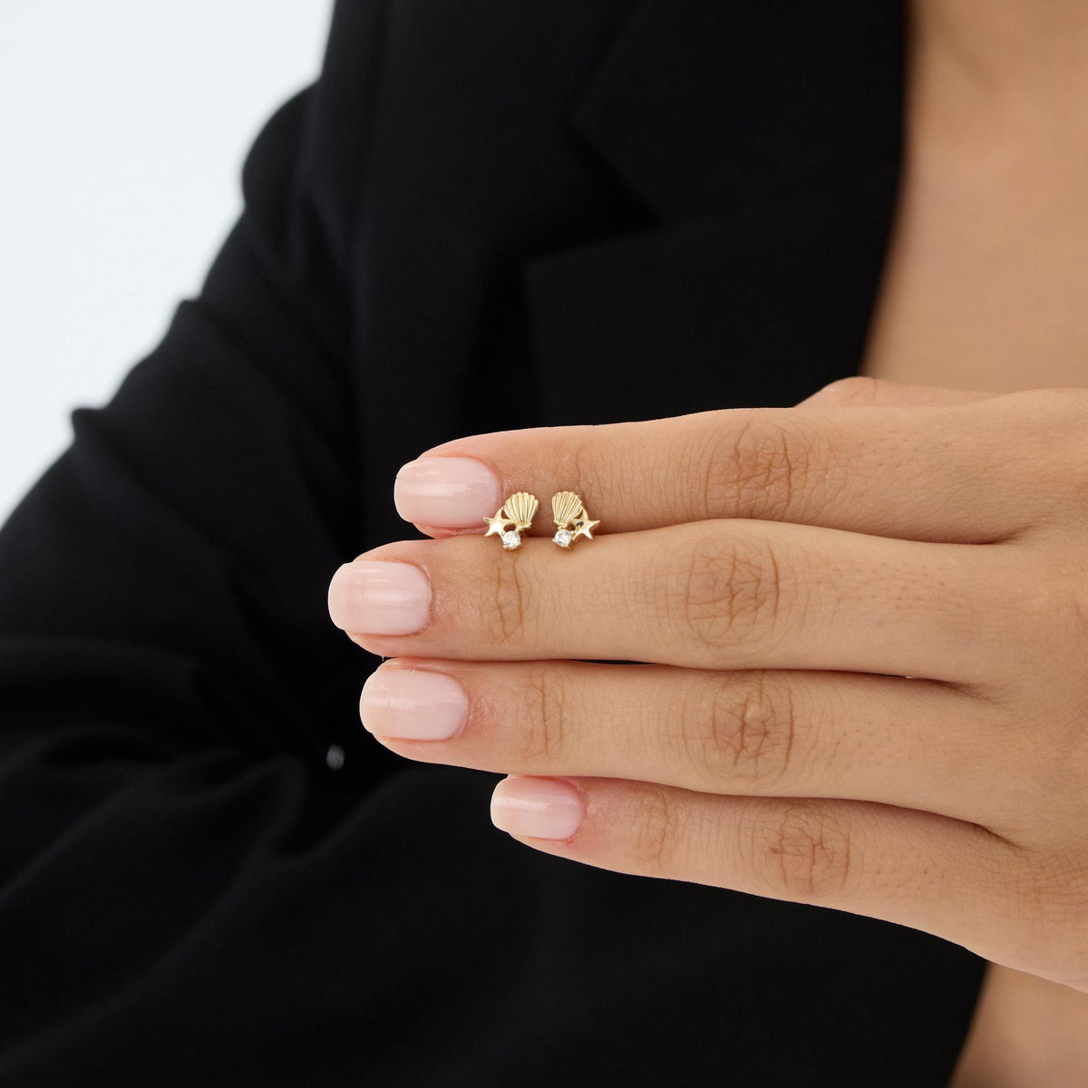 14K gold starfish and shell stud earrings with cubic zirconia held on a fingertip for scale