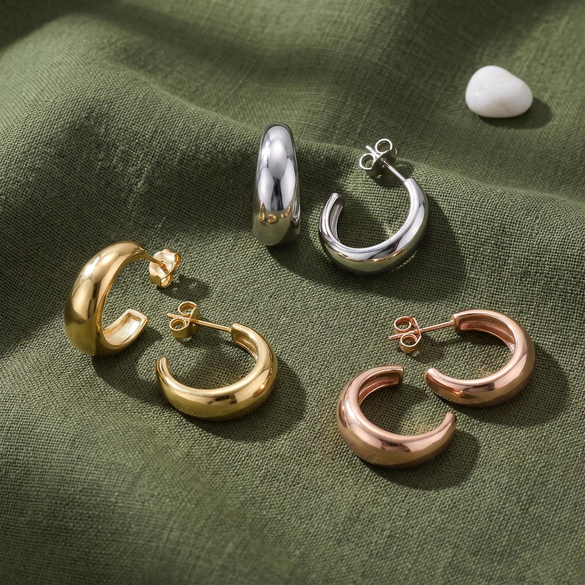 14K gold tapered hoop earrings in yellow, white and rose gold, three pairs on green linen with a white pebble