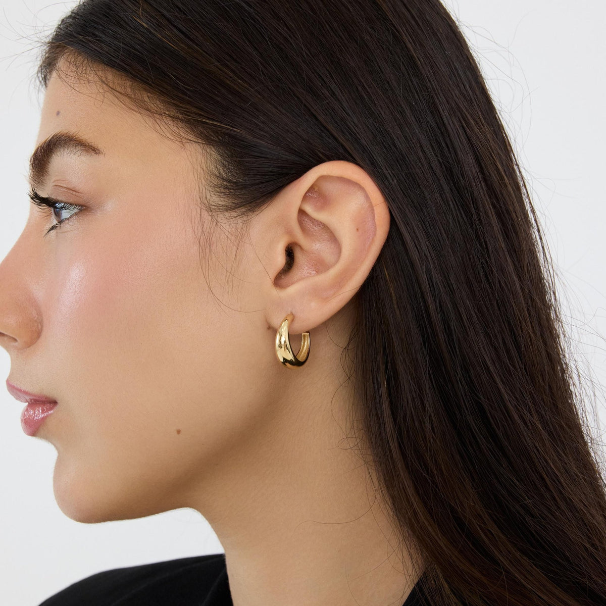 Woman's ear wearing a 14K yellow gold tapered hoop earring, side profile view
