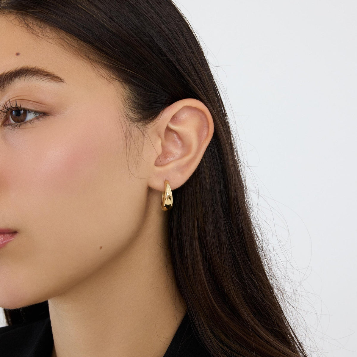 Close-up of a 14K yellow gold tapered hoop earring worn on the ear, viewed from the front-side