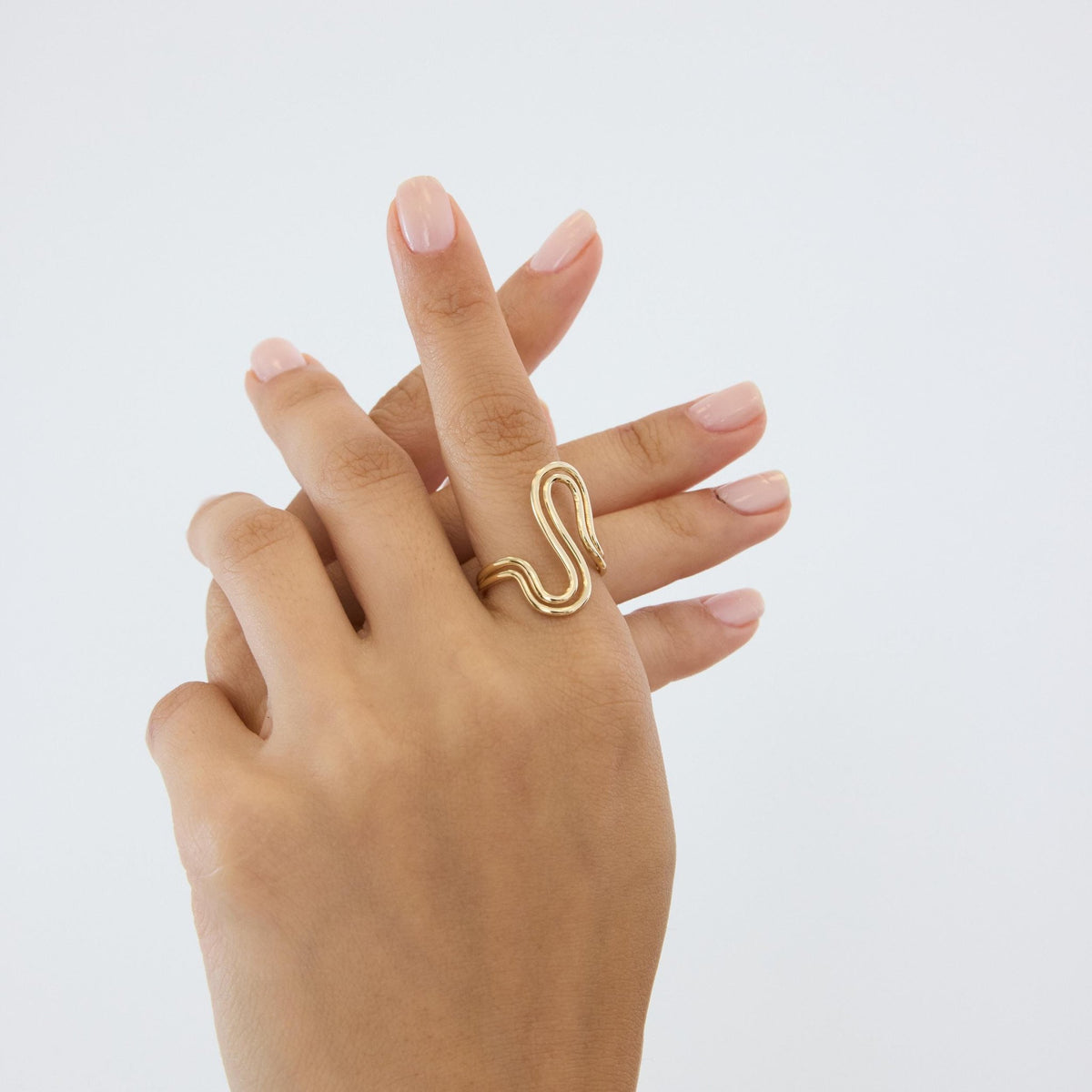 14K gold wave ring worn on the middle finger, hands crossed against a light background
