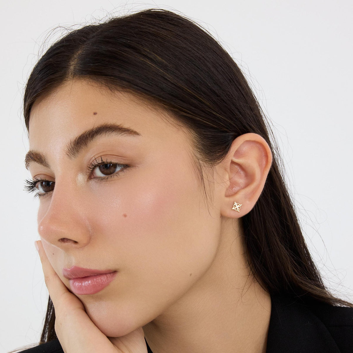 14K gold witch knot stud earring worn in the ear, woman resting her cheek on her hand