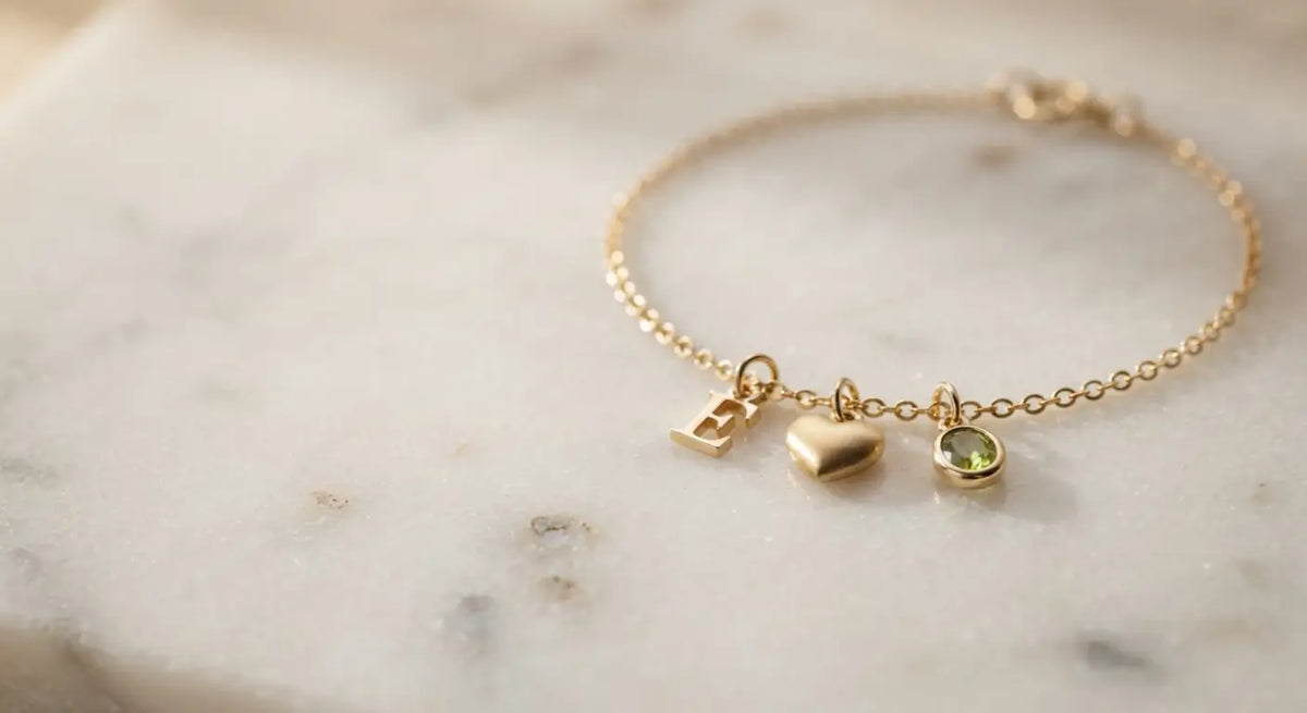 Delicate 14K gold charm bracelet with initial, heart, and birthstone charms on marble